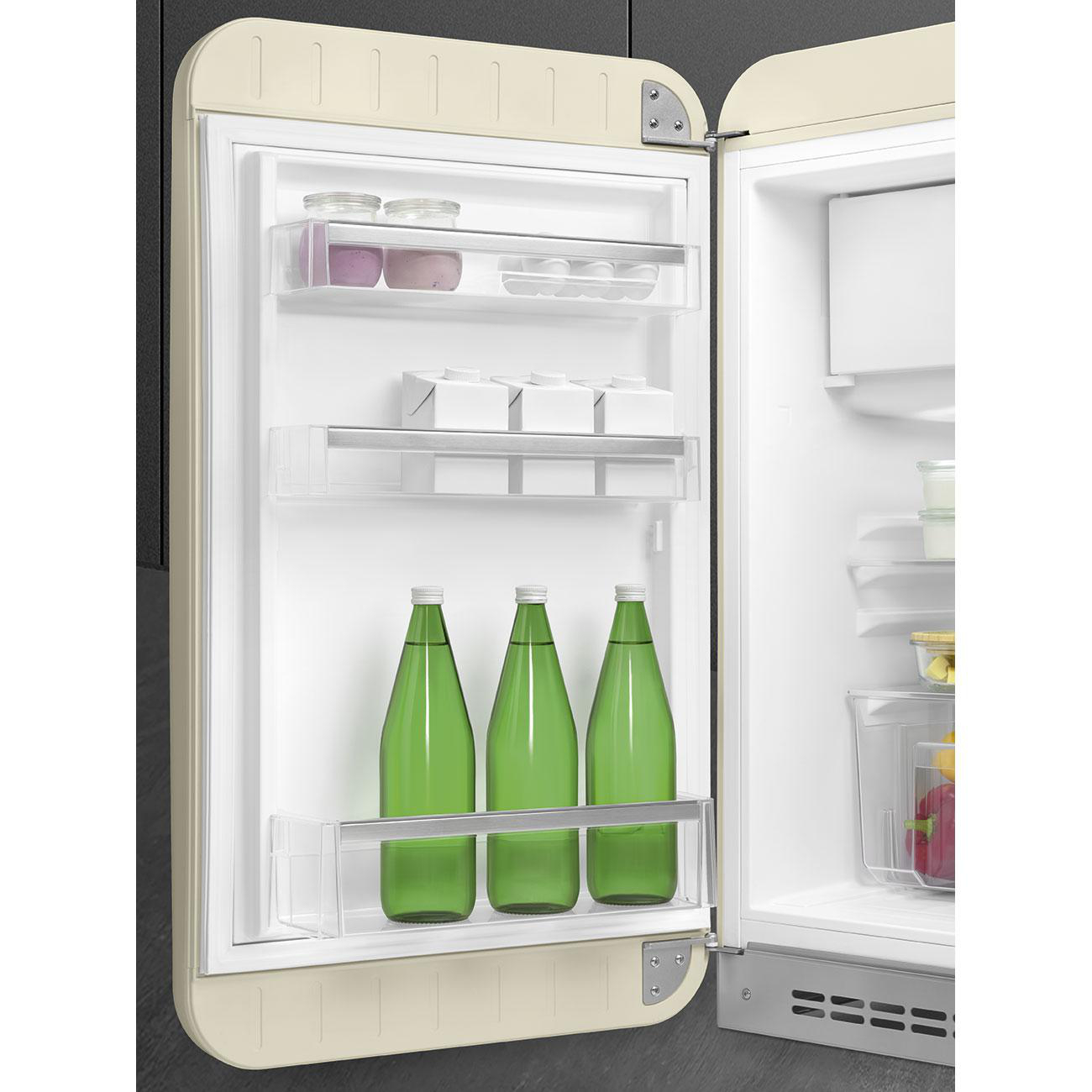 Cremefarbener Retro-Kühlschrank geöffnet, mit Regalen mit Gegenständen, darunter grüne Wasserflaschen.
