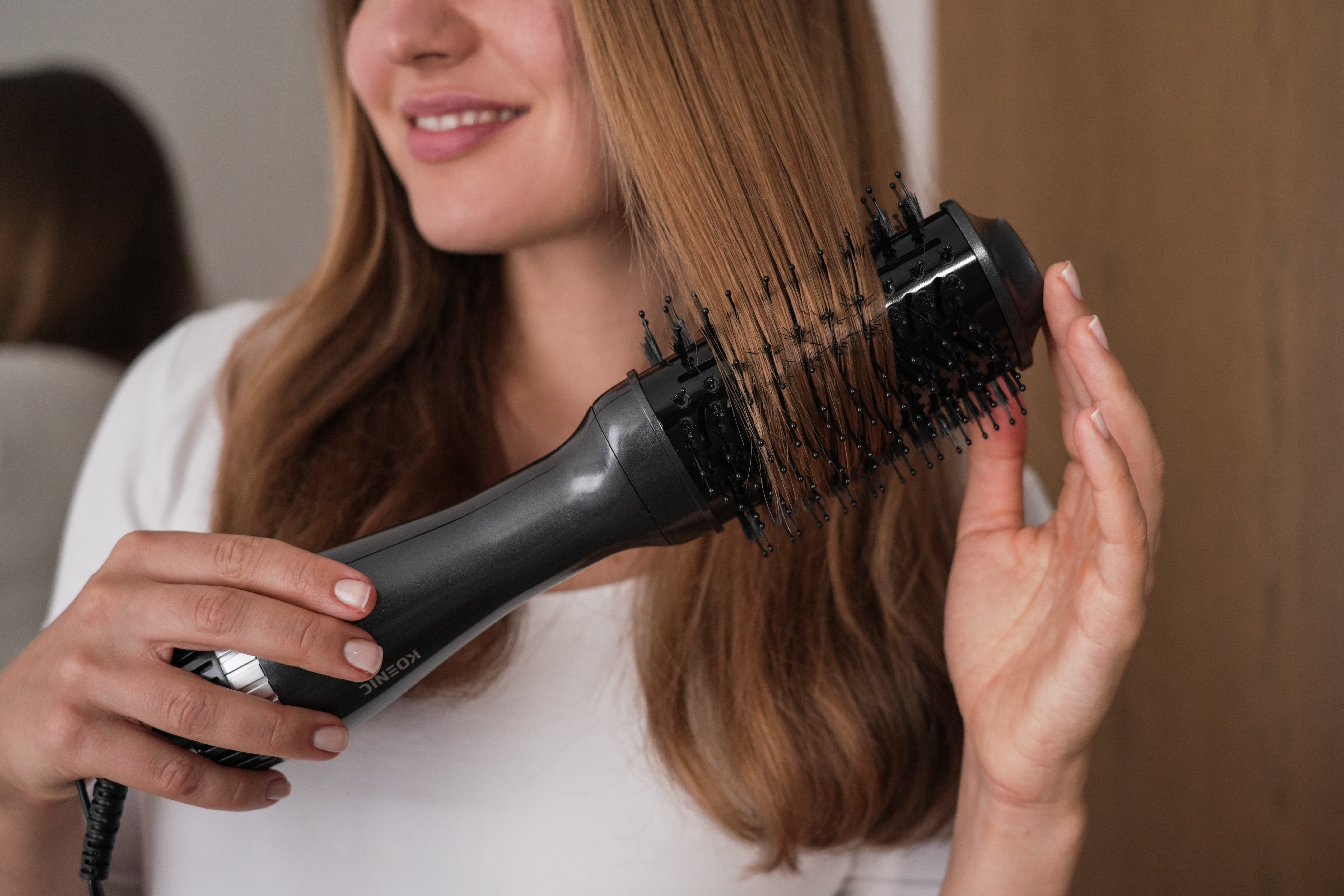 Frau benutzt eine schwarz-graue Haartrocknerbürste für ihr Haar, lächelnd.