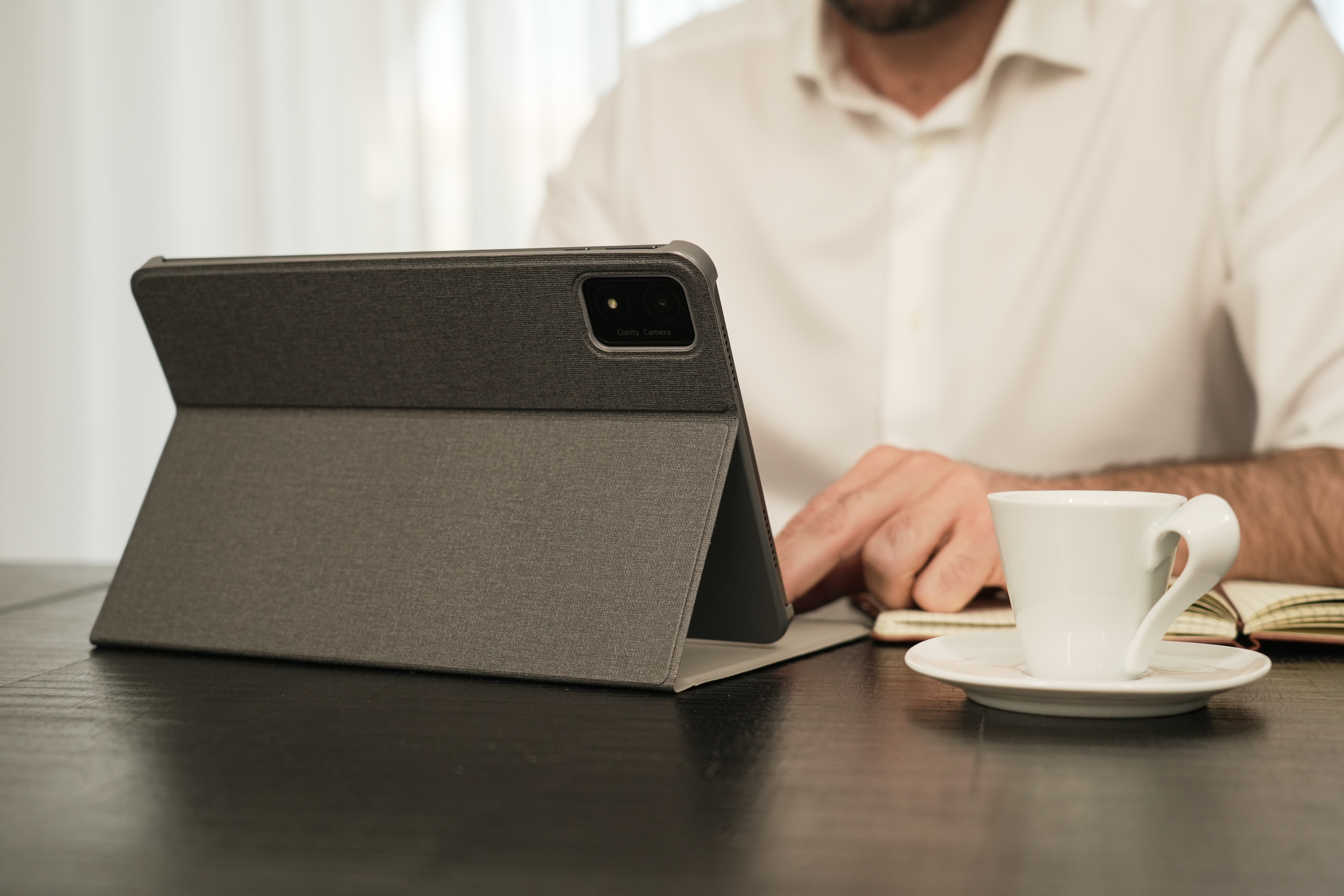 Eine Person arbeitet an einem Tablet mit Hülle auf einem Tisch. Eine Tasse Kaffee ist in der Nähe.