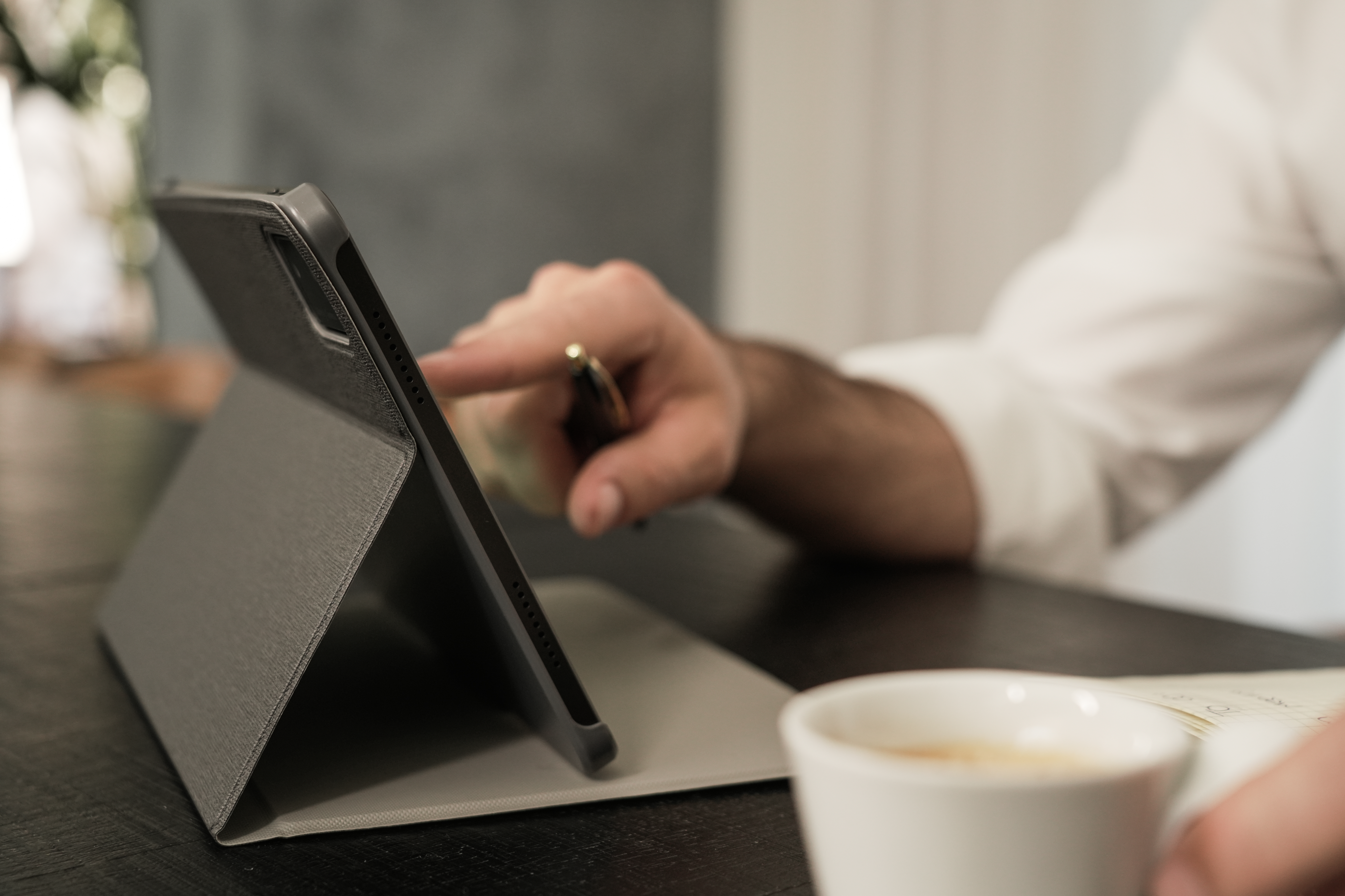 Eine Person benutzt ein Tablet mit Stift auf einer dunklen Oberfläche. Eine Kaffeetasse ist im Vordergrund.
