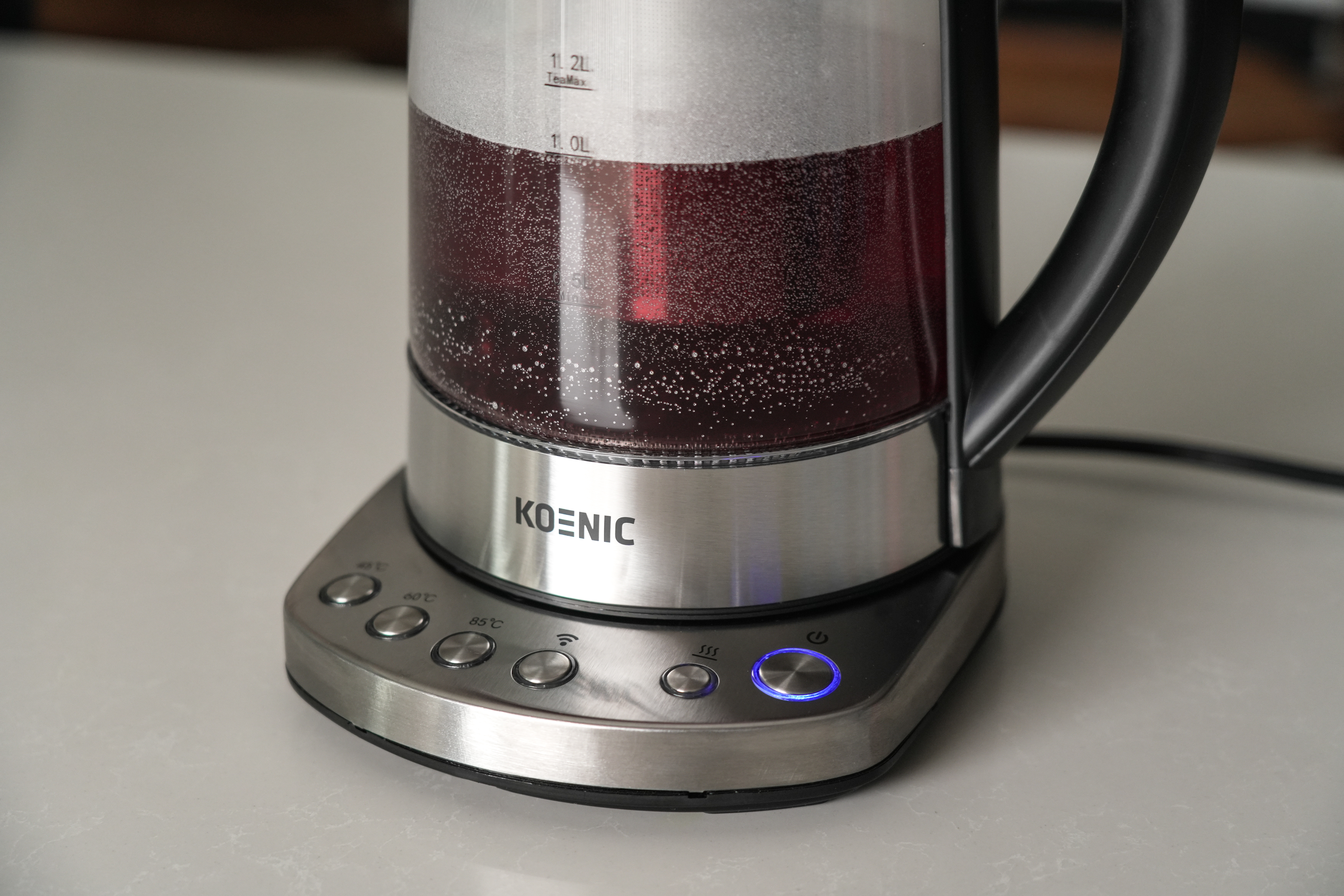 Ein Koenic Wasserkocher mit roter Flüssigkeit, silberner Basis und Knöpfen.
