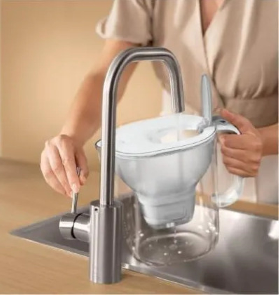 Osoba napełniająca dzbanek filtrujący wodę w zlewie, ze srebrną baterią.
