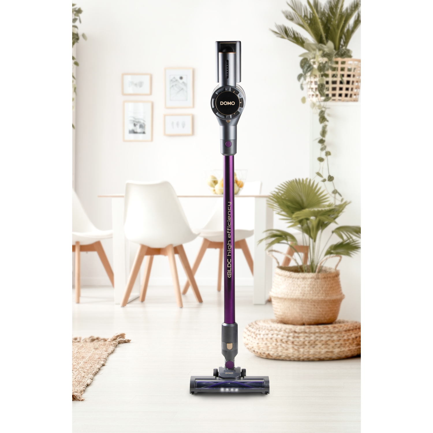 Un aspirateur sans fil violet et gris se tient dans une pièce lumineuse avec une table à manger et des plantes.