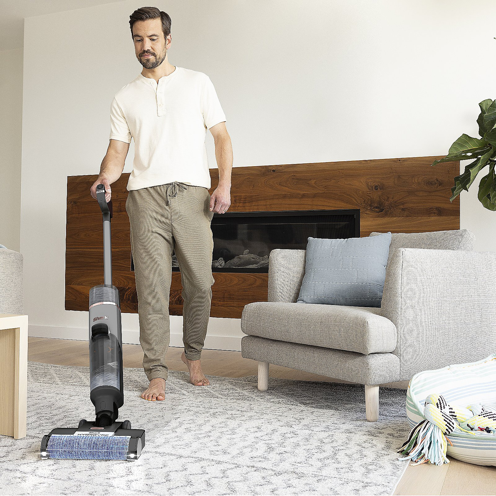 Homme passant l'aspirateur sur un tapis avec un aspirateur Shark, dans un salon.