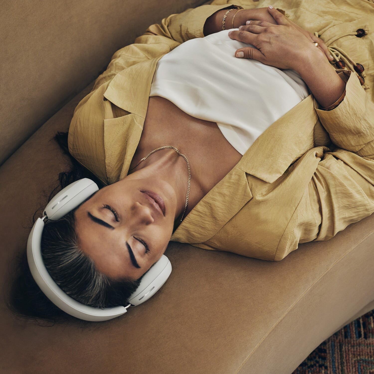 A woman lies on a couch wearing headphones, a white shirt, and a yellow jacket.