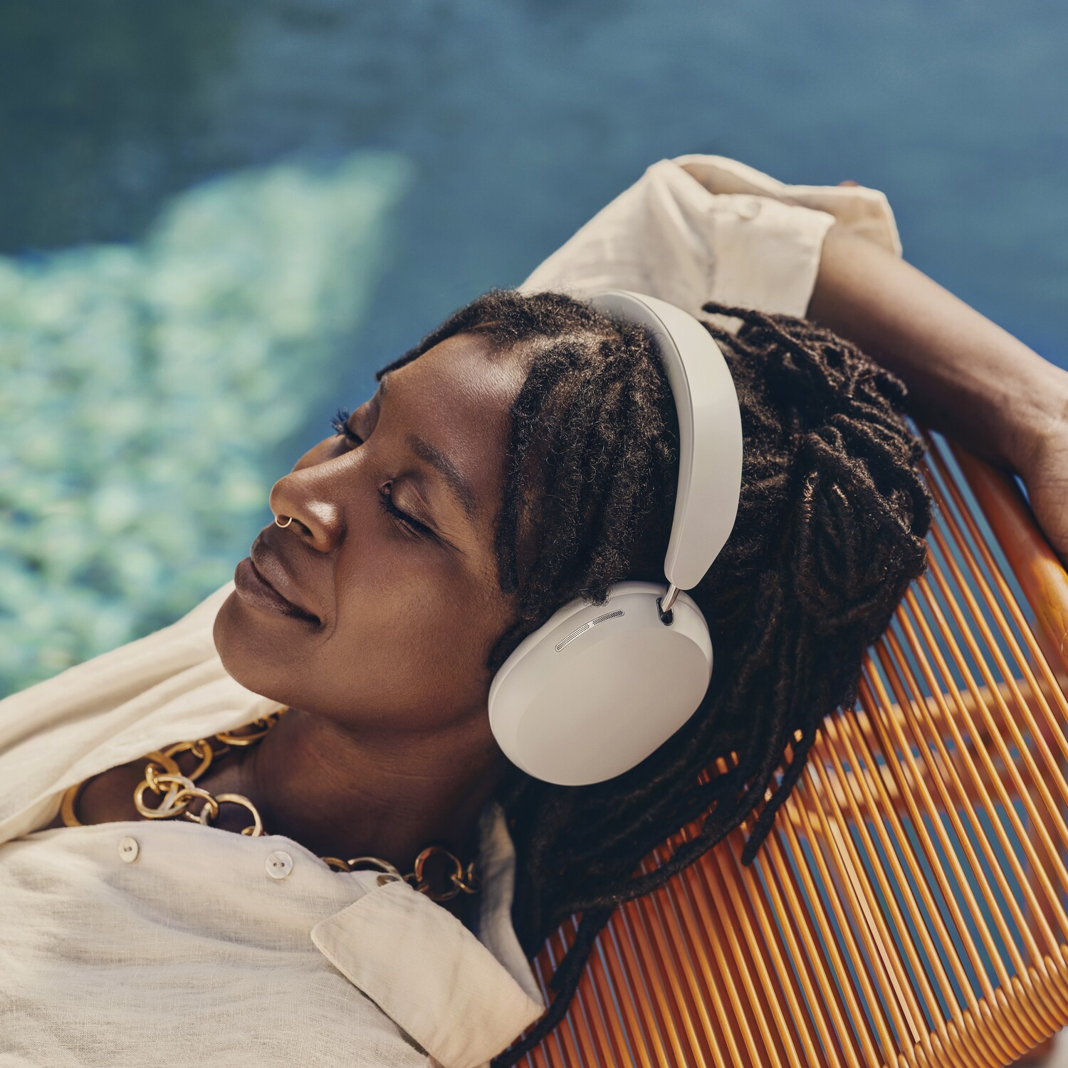 A woman with headphones rests on a chair near a pool.