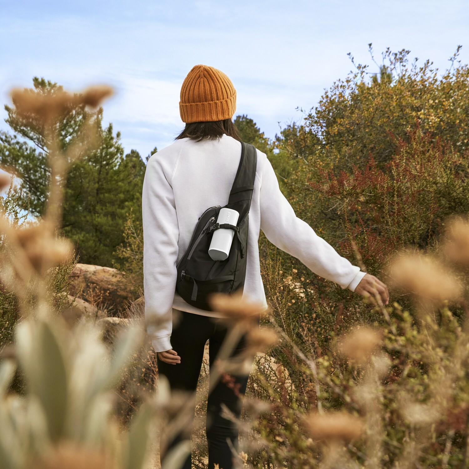 A person hikes through a trail with a backpack, wearing a beanie, and a white sweater.