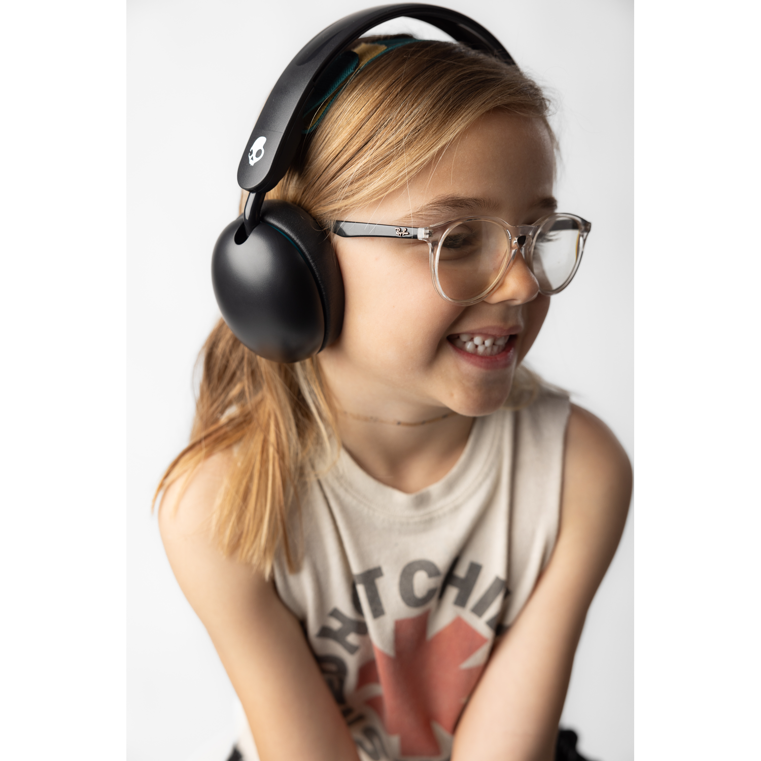 A young girl smiles wearing black headphones and glasses.