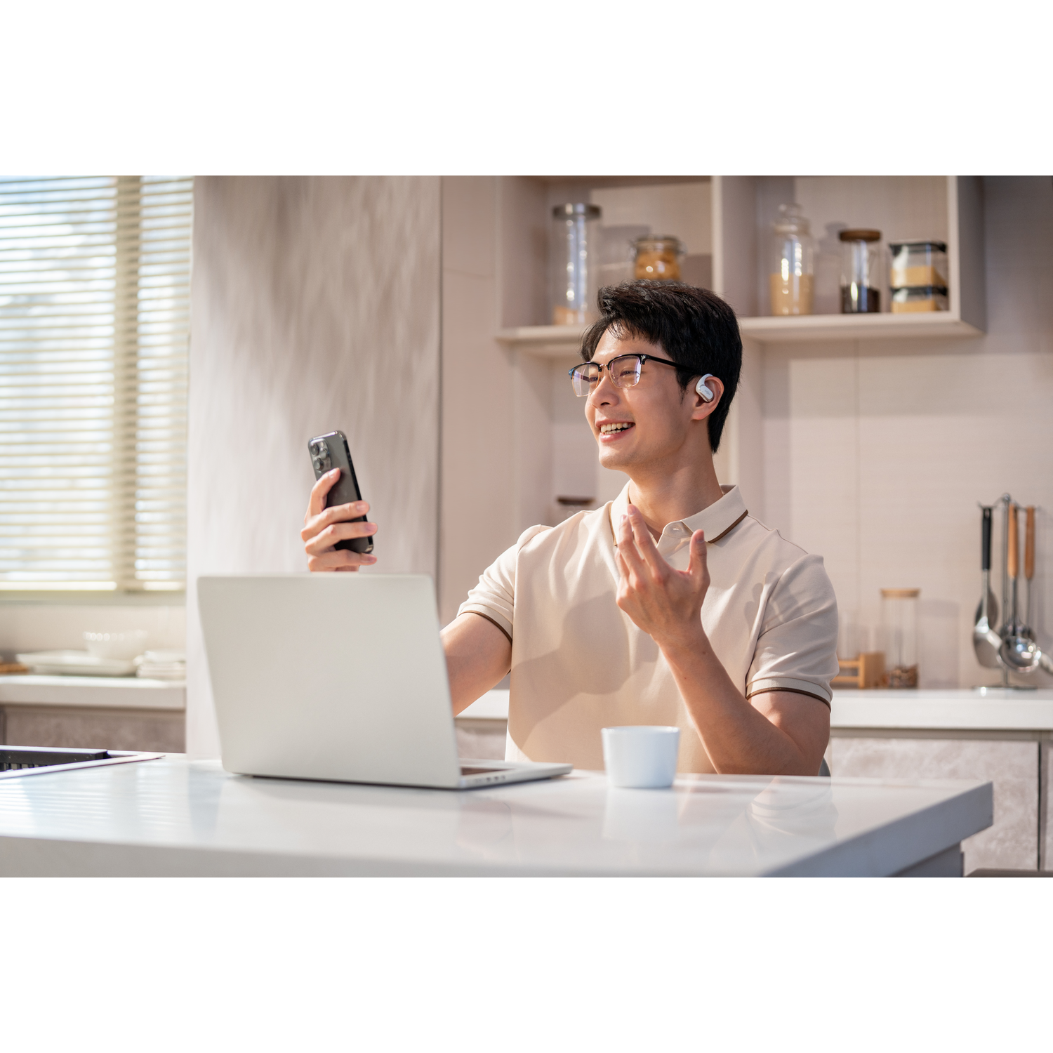 Man wearing earbuds, smiling, holding a phone in a kitchen setting.
