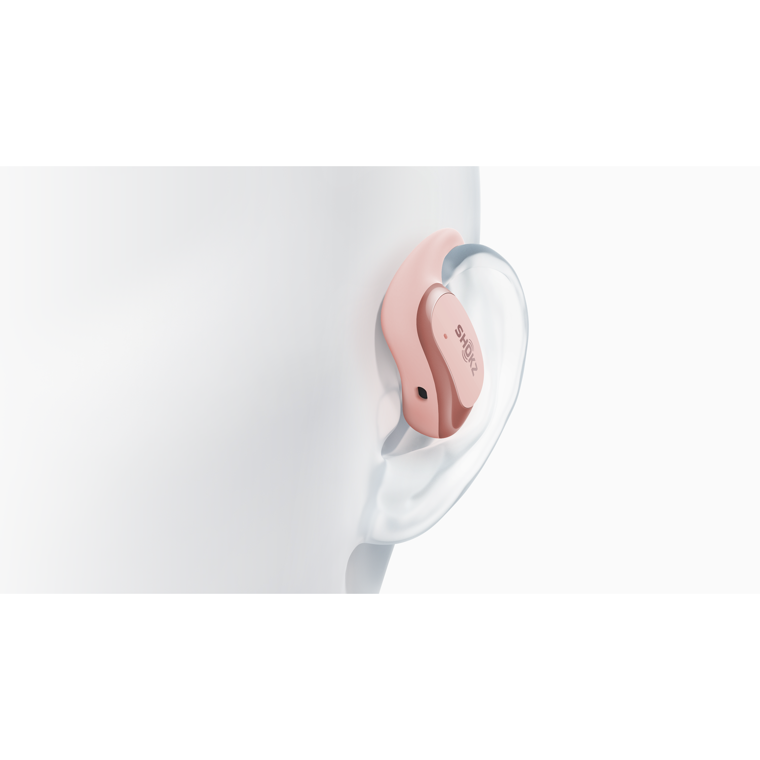 A pink hearing aid is placed in a person's ear. The Shokz logo is visible on the hearing aid.