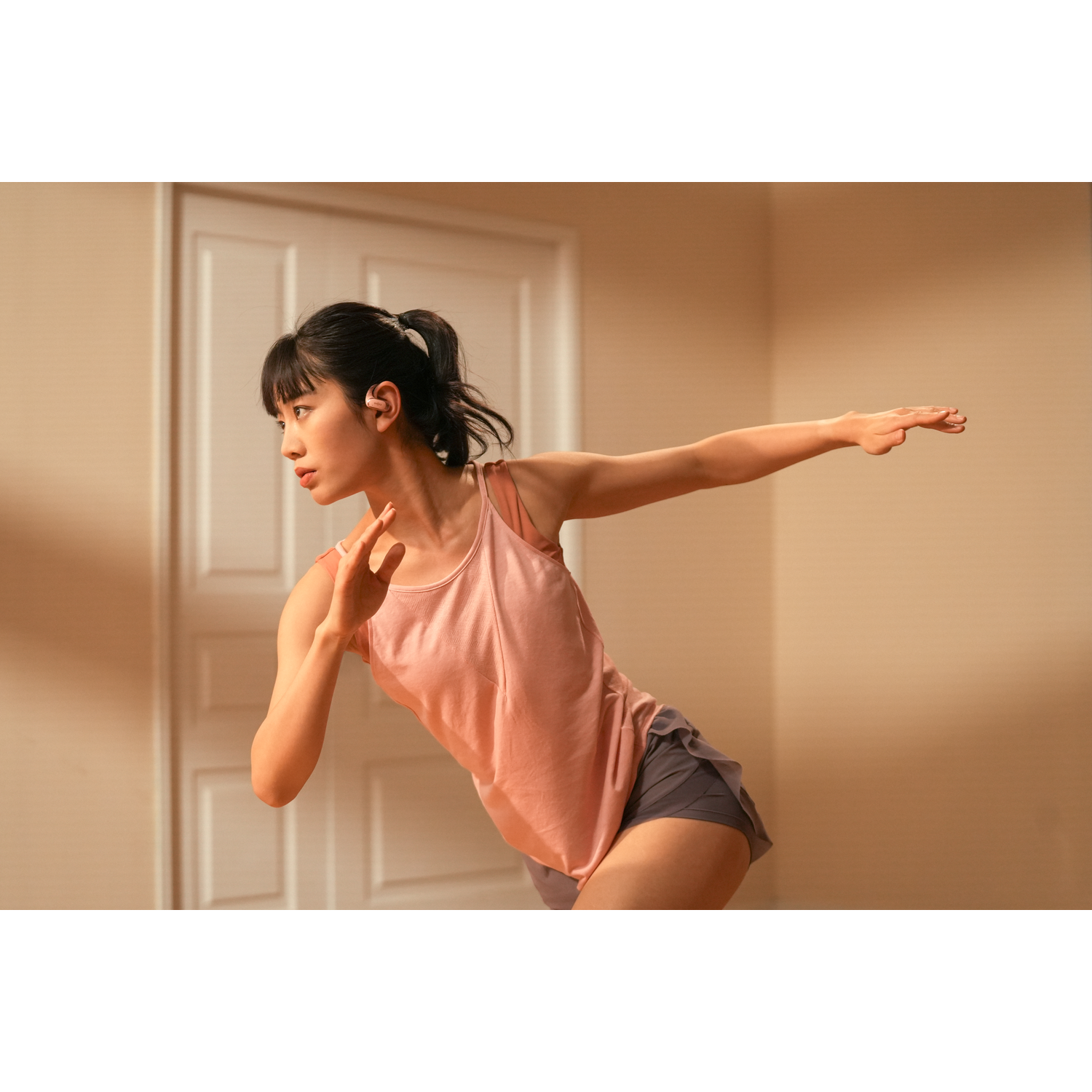 Woman wearing earbuds, dancing with arms outstretched in a room.