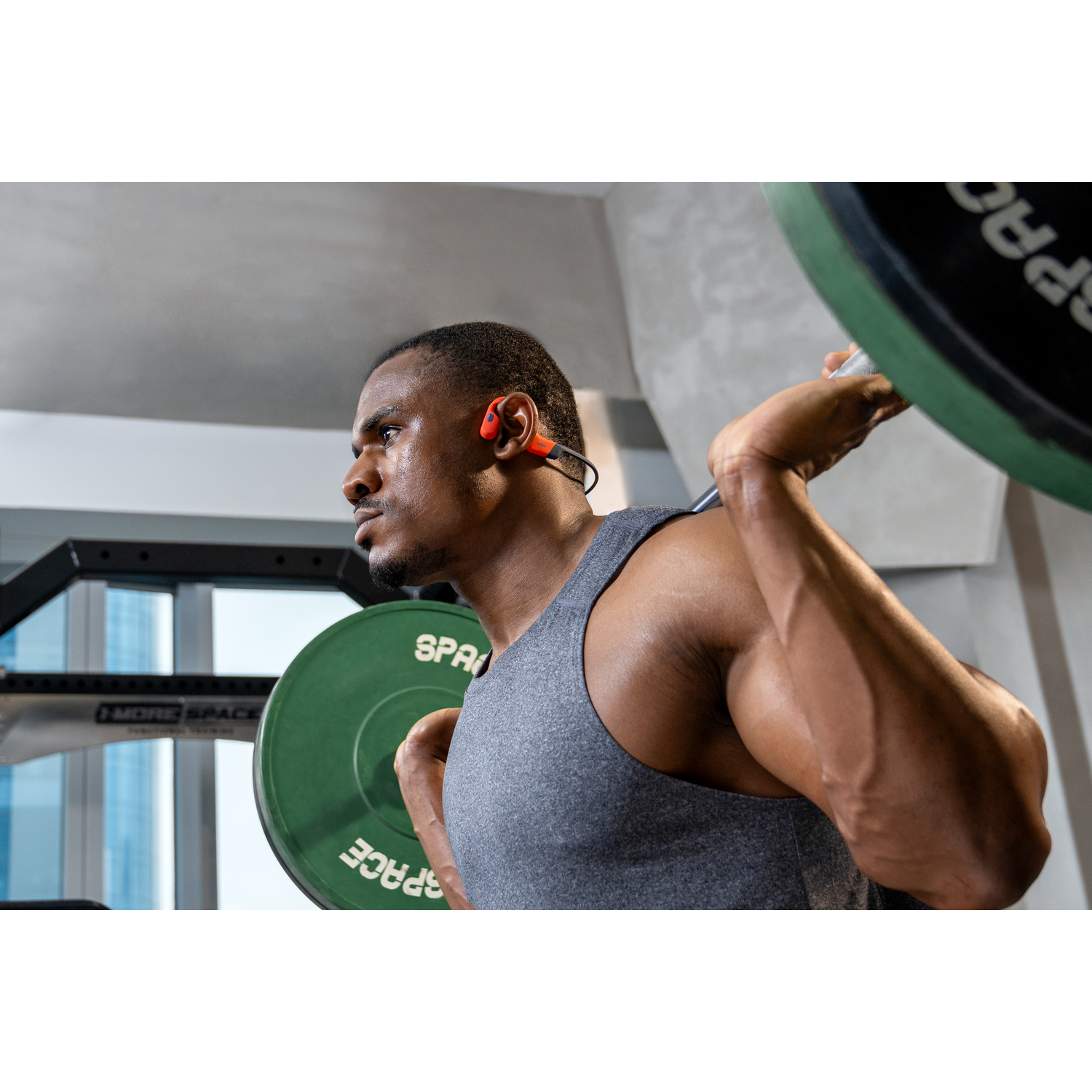 Man lifting weights, wearing headphones. Gym setting with green weights and grey background.