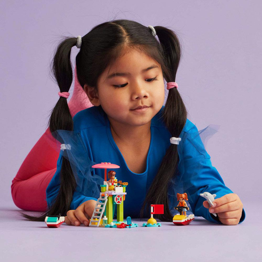 Ein junges Mädchen spielt mit Lego-Spielzeug. Sie liegt auf dem Boden, umgeben von Lego.