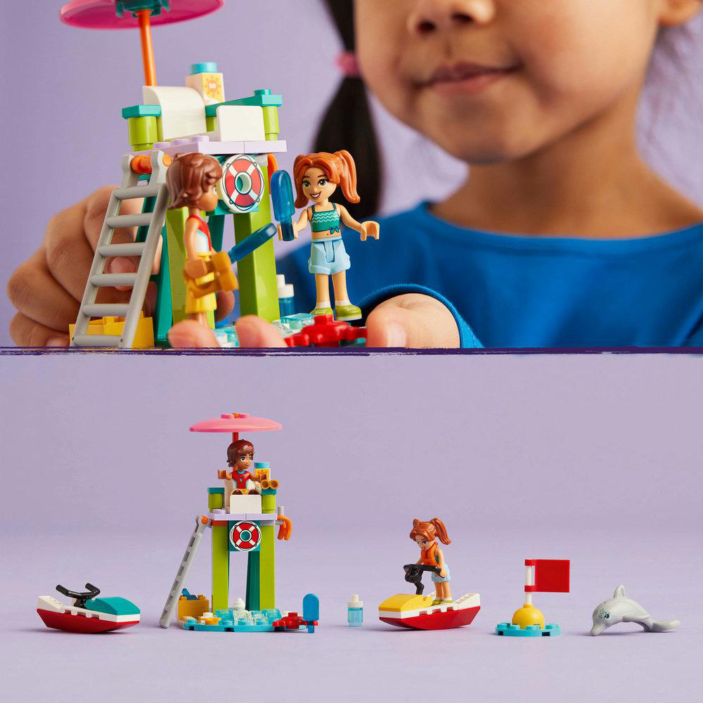 Lego-Set mit Figuren in einer Strandszene mit einem Rettungsturm, ein Kind hält das Set.