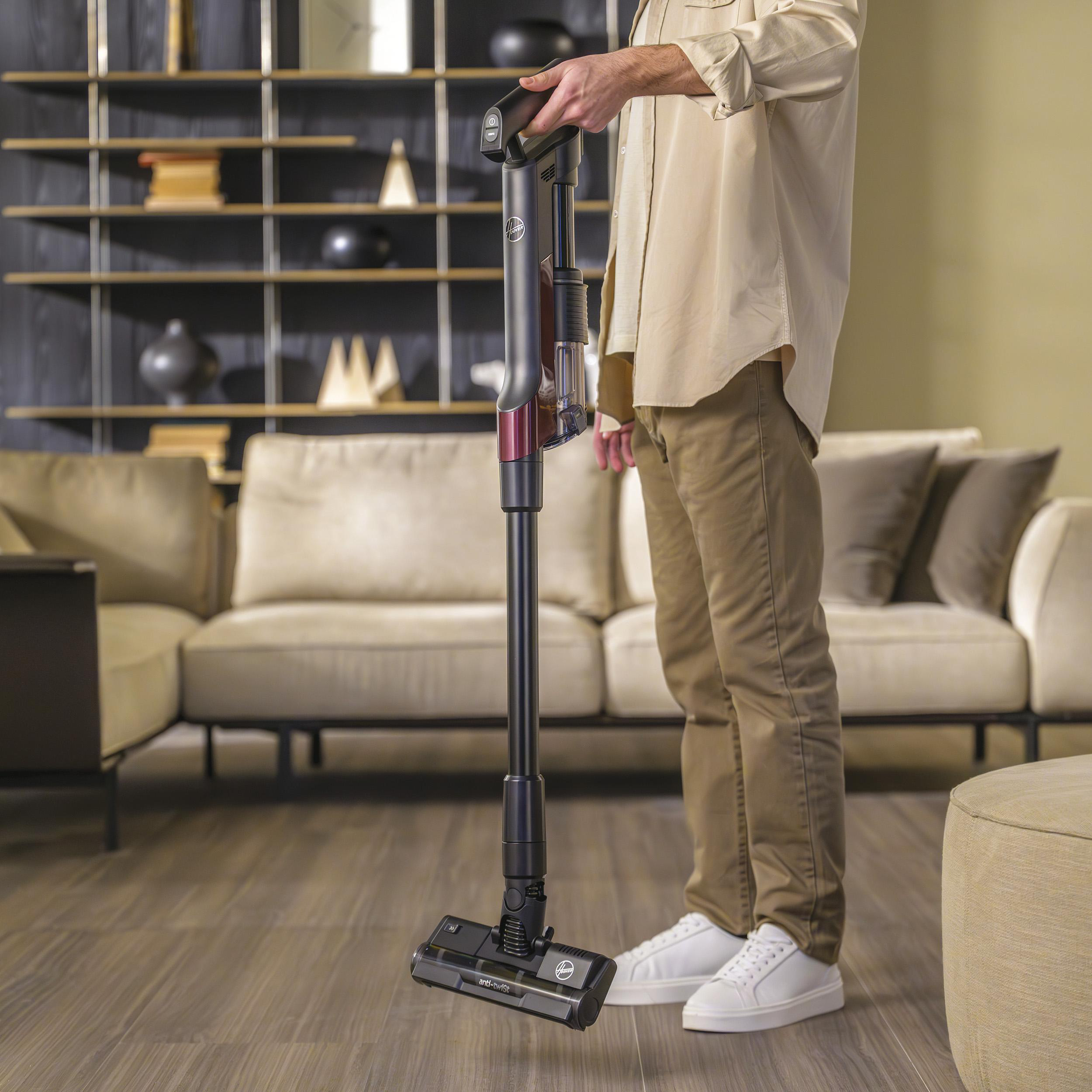 Mann, der einen kabellosen Staubsauger in einem Wohnzimmer benutzt. Holzboden und Sofa.