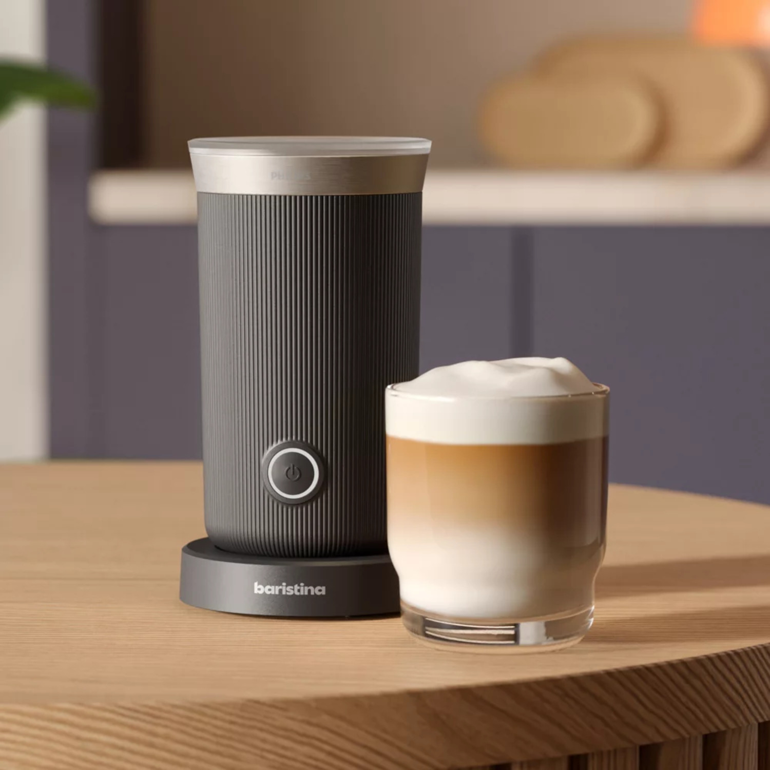 A grey and silver milk frother and a glass of latte on a wooden table. Kitchen background.