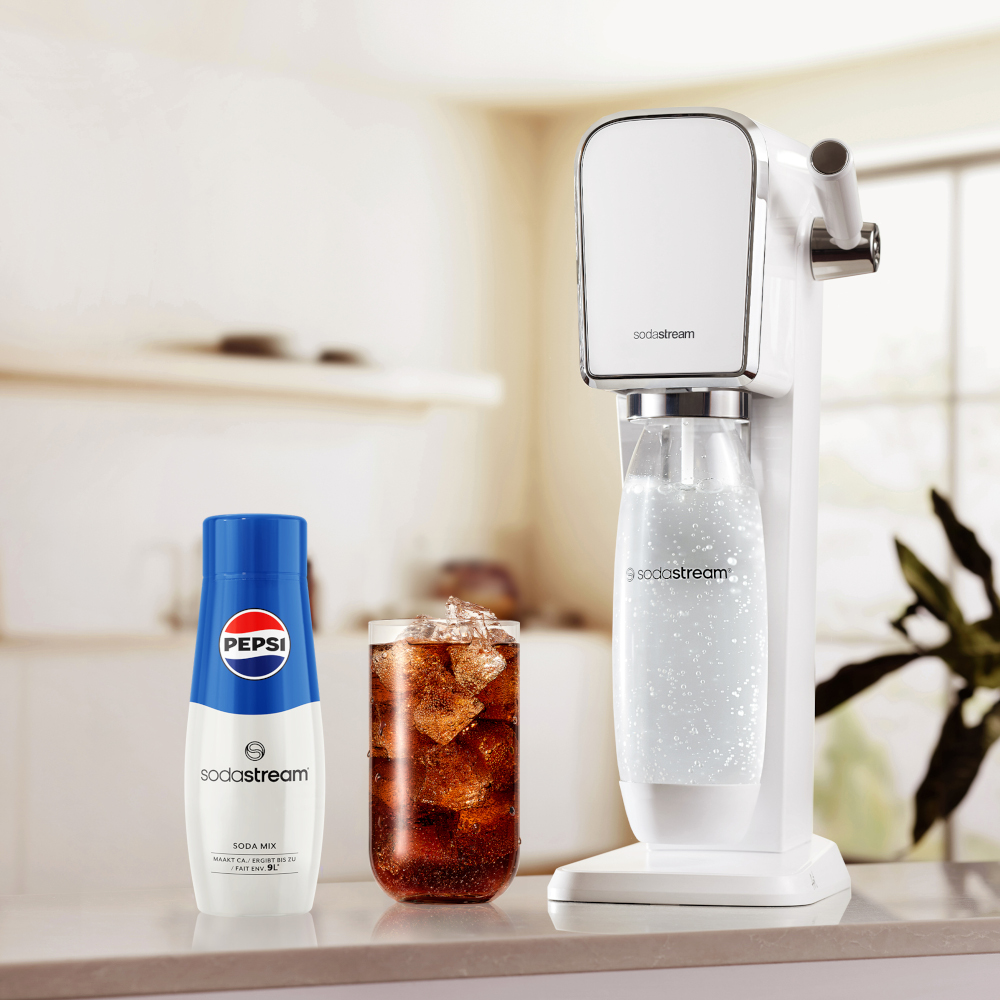White SodaStream machine with a Pepsi soda mix and a glass of soda on a counter.