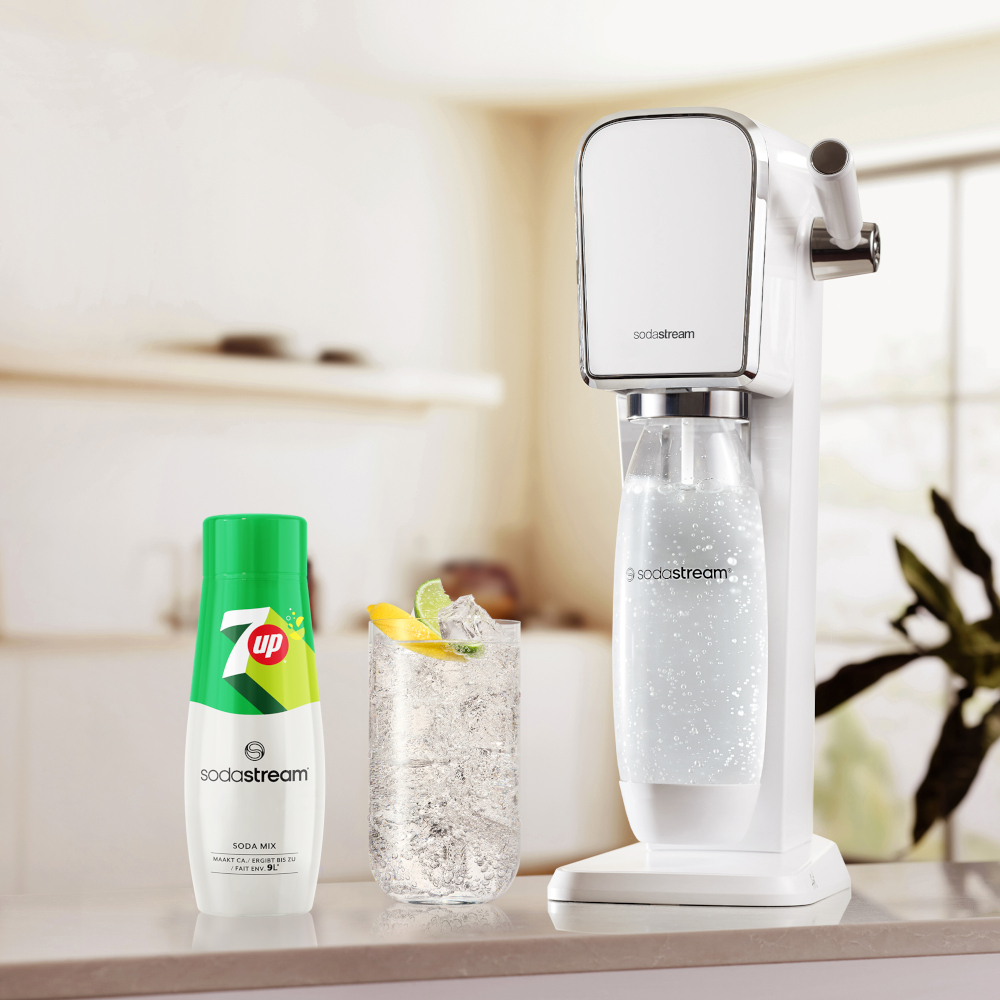 White soda maker, a 7up soda mix, and a glass of soda with a lemon slice.