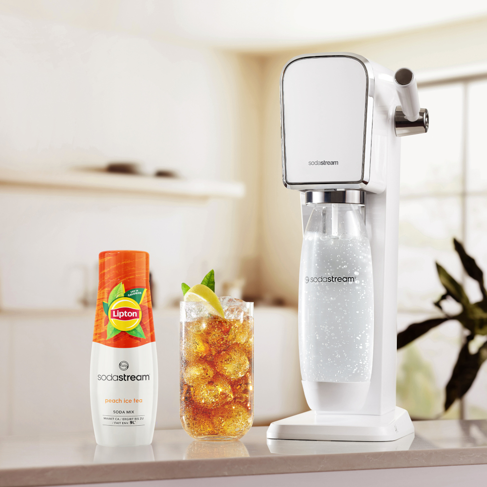 White soda machine, a glass of peach ice tea and a bottle of soda mix on a surface.