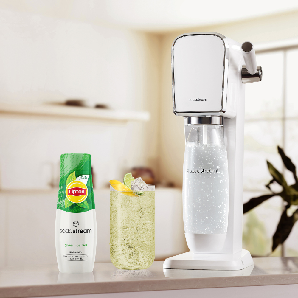 Machine à soda blanche, bouteille de thé glacé vert, verre avec citron et glace, le tout sur un comptoir.