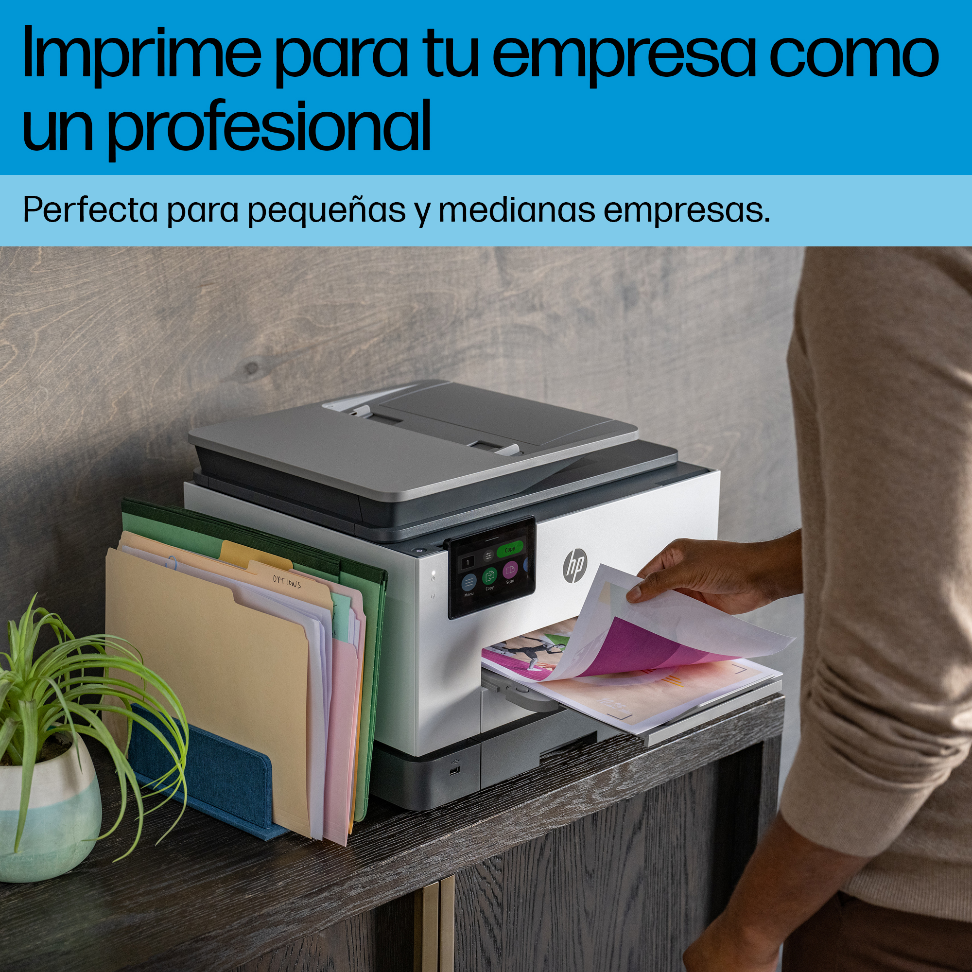 Una persona está usando una impresora, con varias carpetas de archivos de colores en un escritorio.