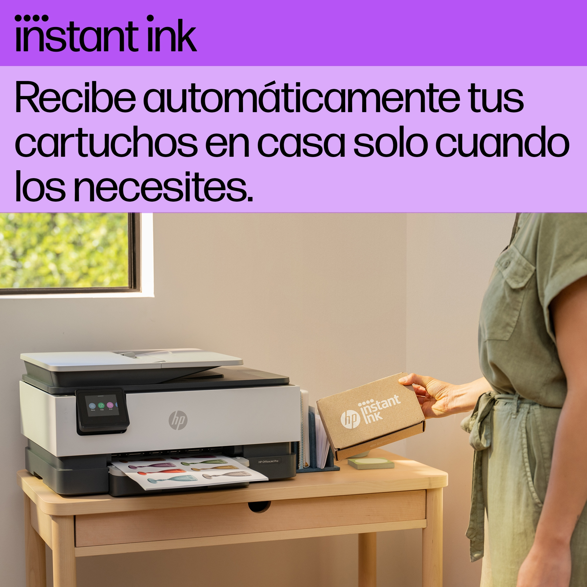 Una mujer toma una caja de una impresora. Texto: 'instant ink'. Impresora en un escritorio.