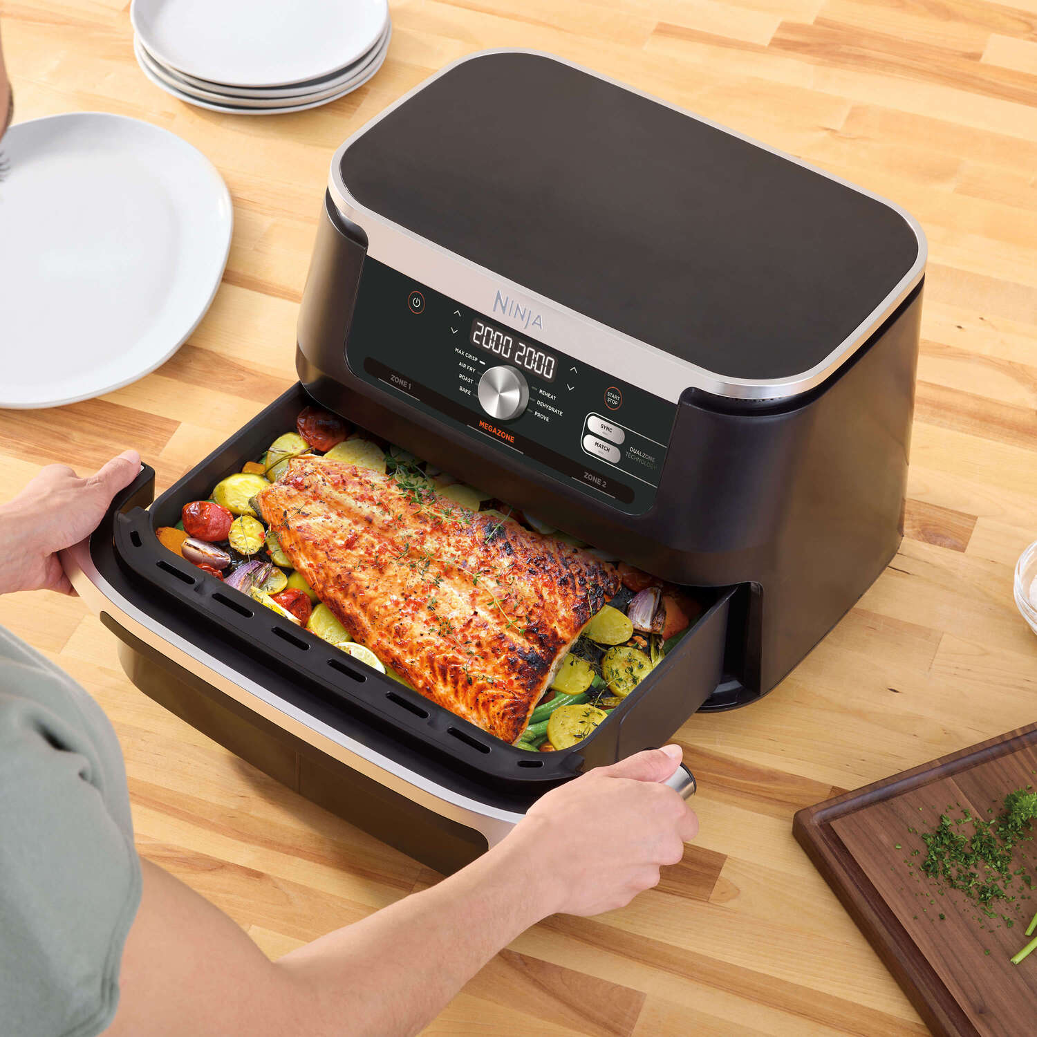Airfryer met zalm en groenten. Persoon trekt de lade eruit.