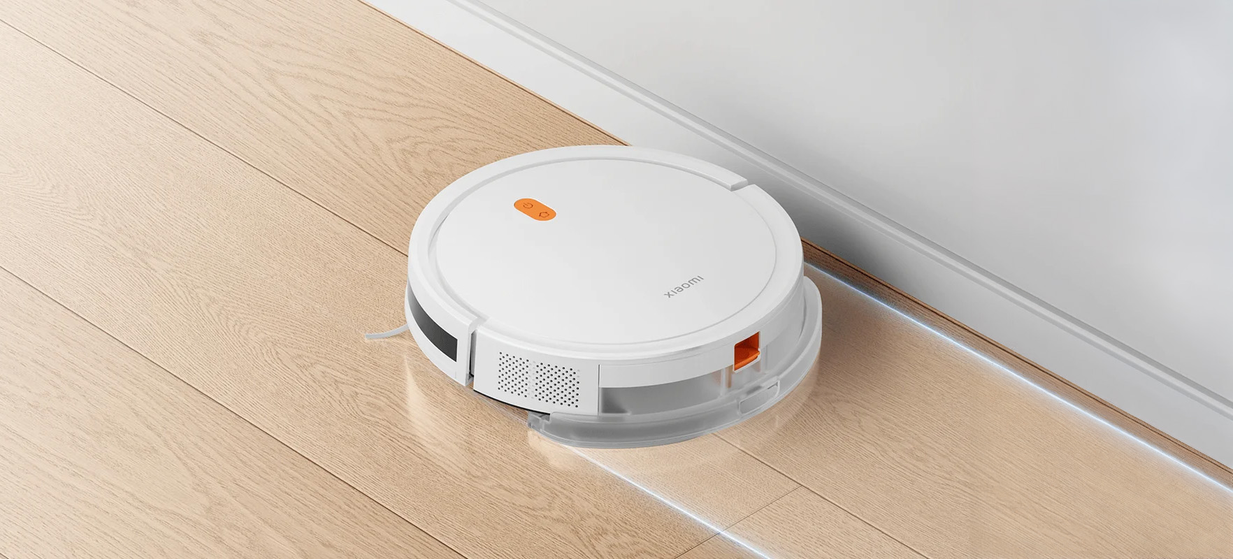 Biały robot sprzątający Xiaomi na drewnianej podłodze, w pobliżu białej ściany.