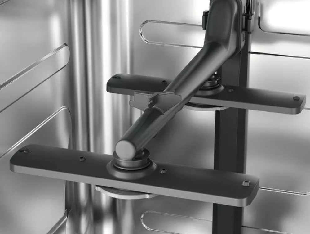 Wnętrze zmywarki. Dwa szare ramiona natryskowe na tle wnętrza ze stali nierdzewnej.