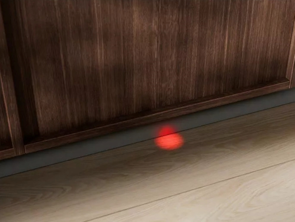 Czerwone światło świeci na drewnianą podłogę, w pobliżu dolnej części brązowej szafki.