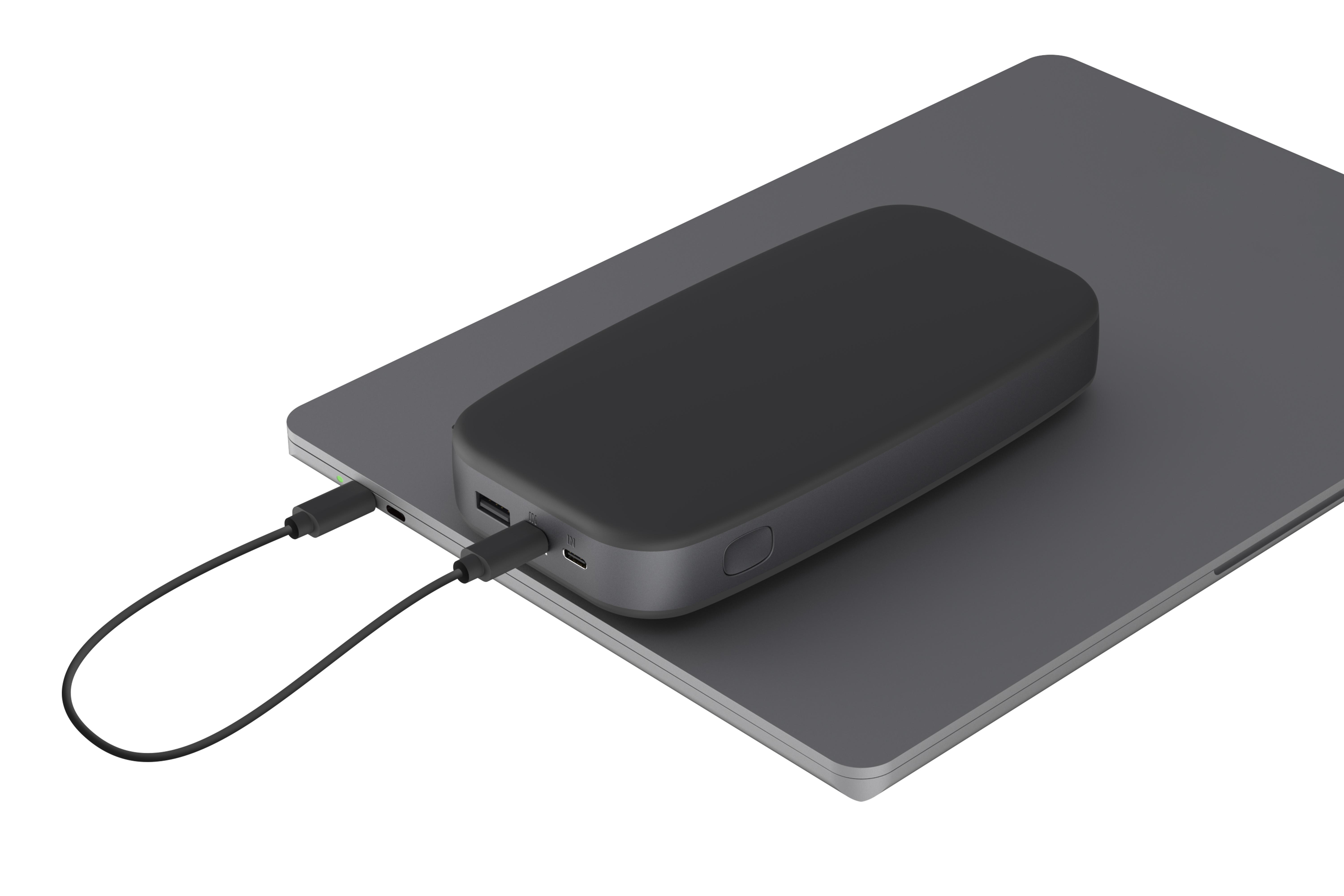Eine schwarze Powerbank lädt einen grauen Laptop. Ein schwarzes Kabel verbindet die Geräte.