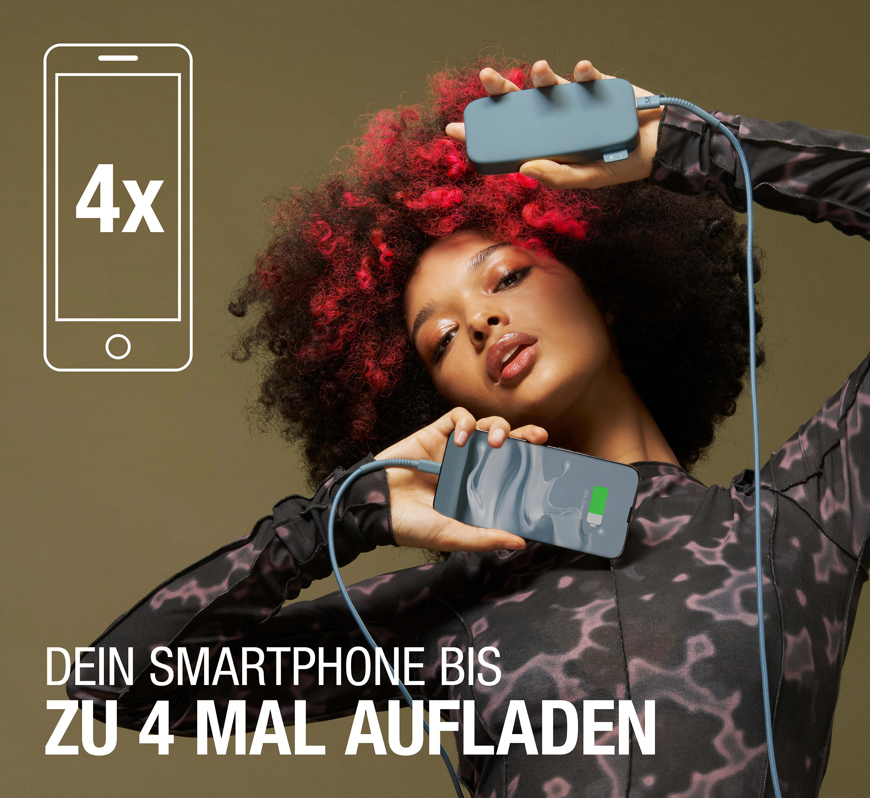 Eine Frau mit roten Haaren hält eine Powerbank, neben einem Telefon, das mit einem Kabel geladen wird.