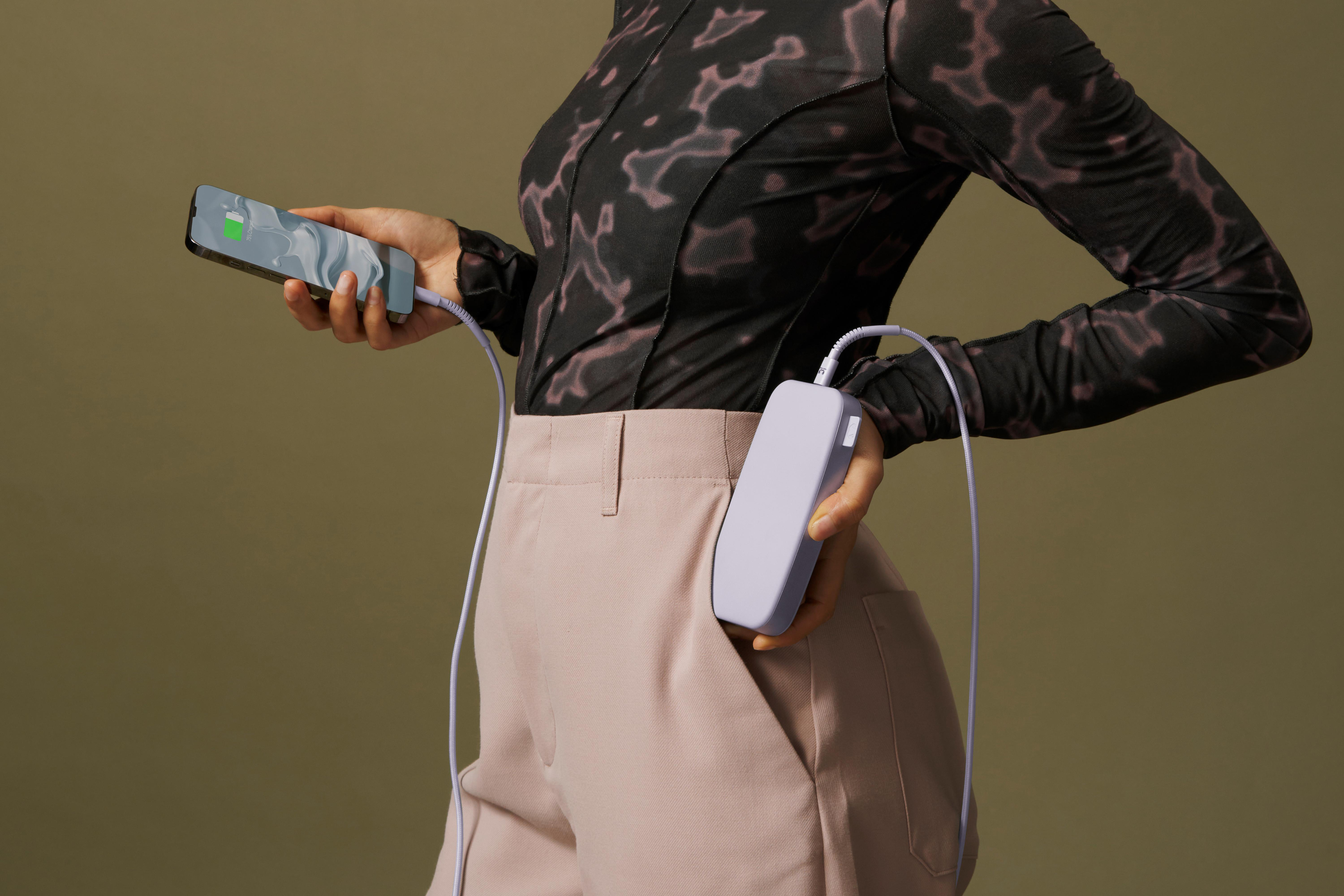 Frau hält ein Telefon, das von einer Powerbank in ihrer Tasche geladen wird. Der Hintergrund ist grün.