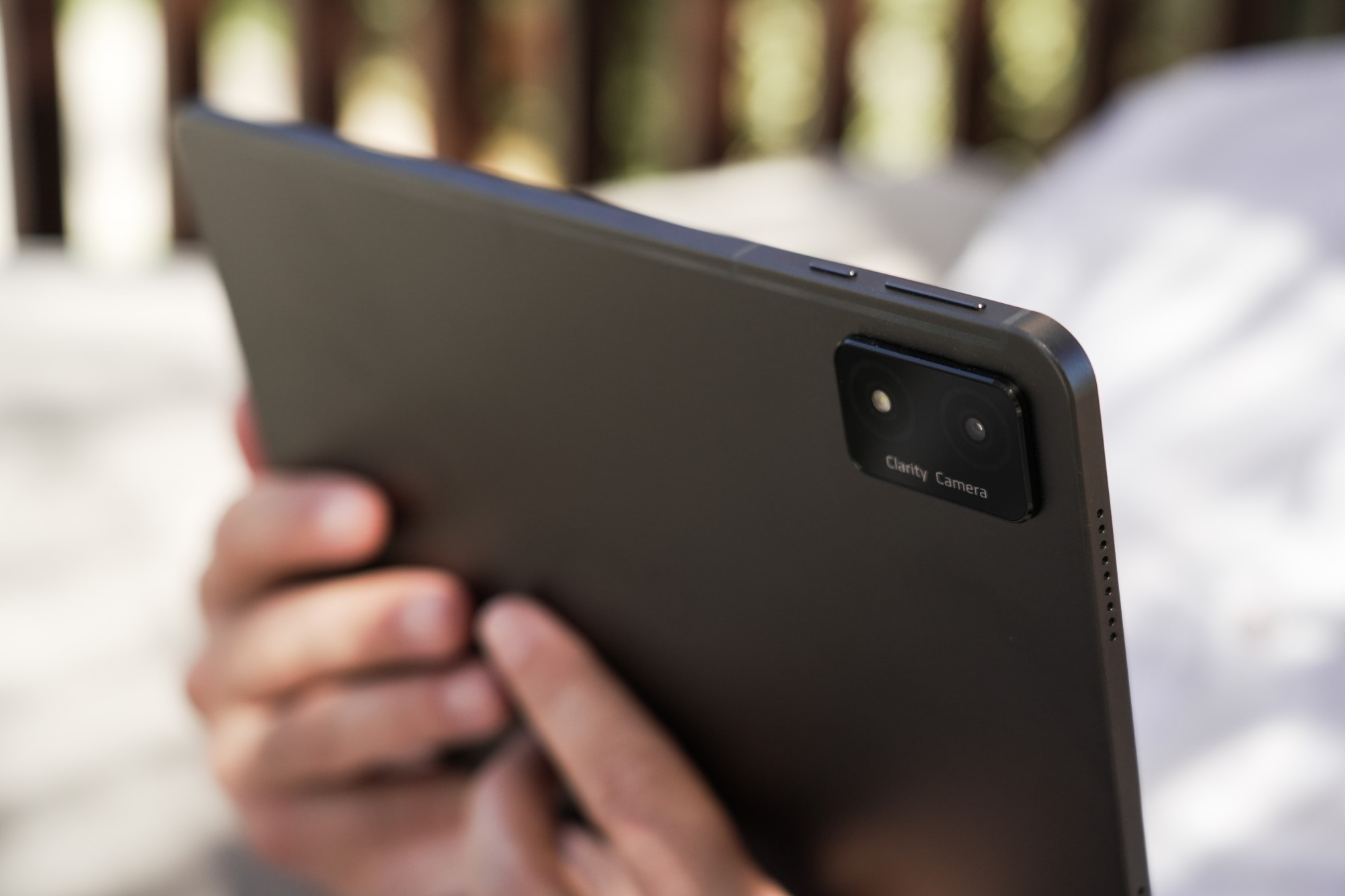 Ciemny tablet trzymany w dłoniach, pokazujący tył. Widoczna jest kamera i tekst 'Clarity Camera'.