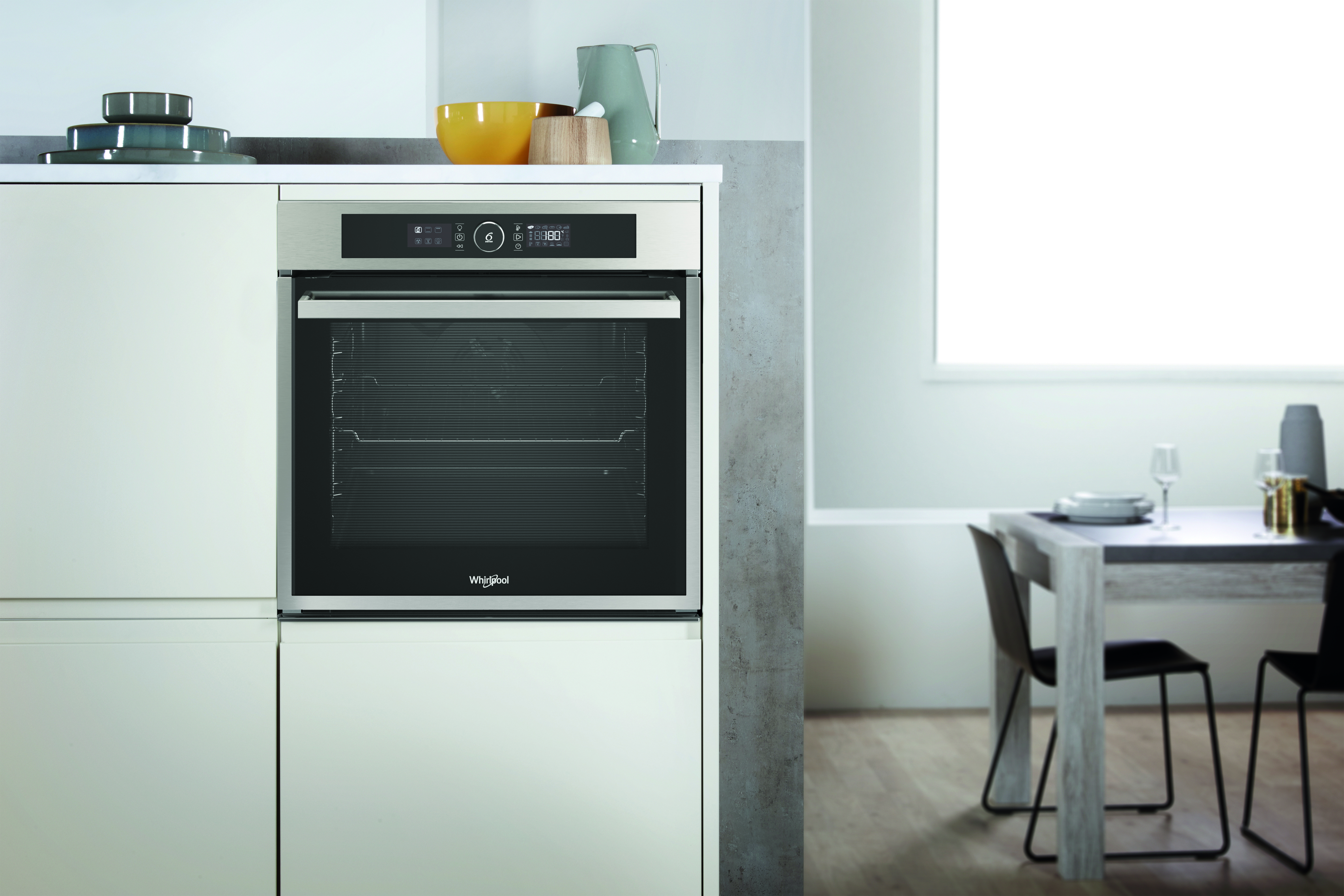 Un horno empotrado en un mueble de cocina. En el fondo hay una mesa de comedor y una ventana.