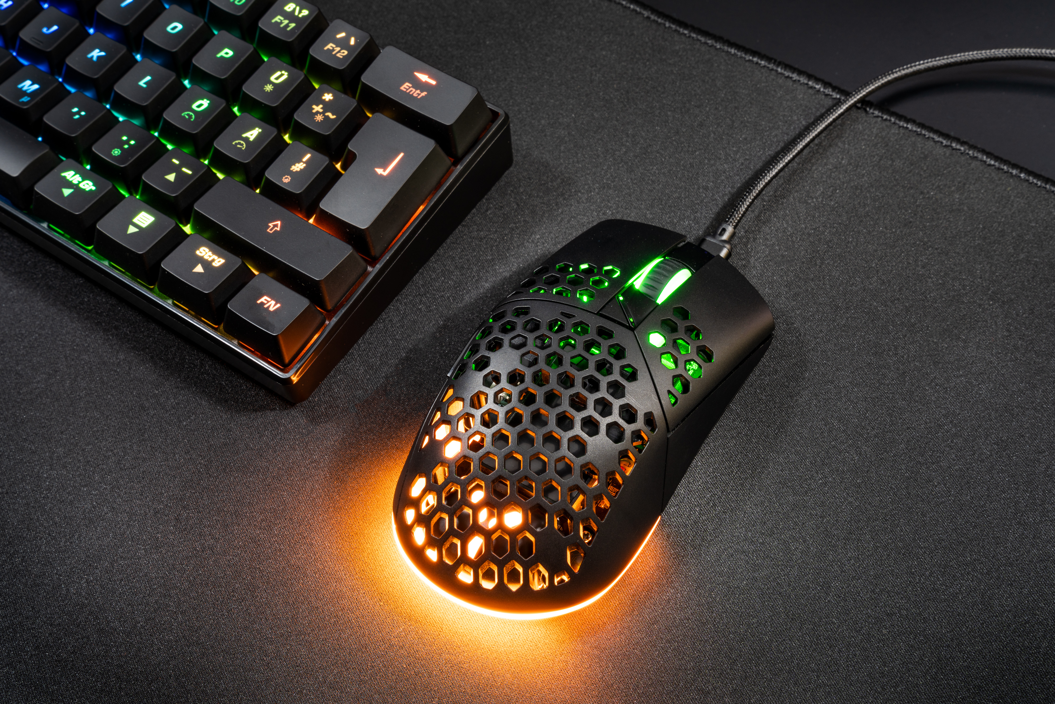Gaming-Maus mit Wabenmuster, orange und grün beleuchtet, und eine Tastatur.