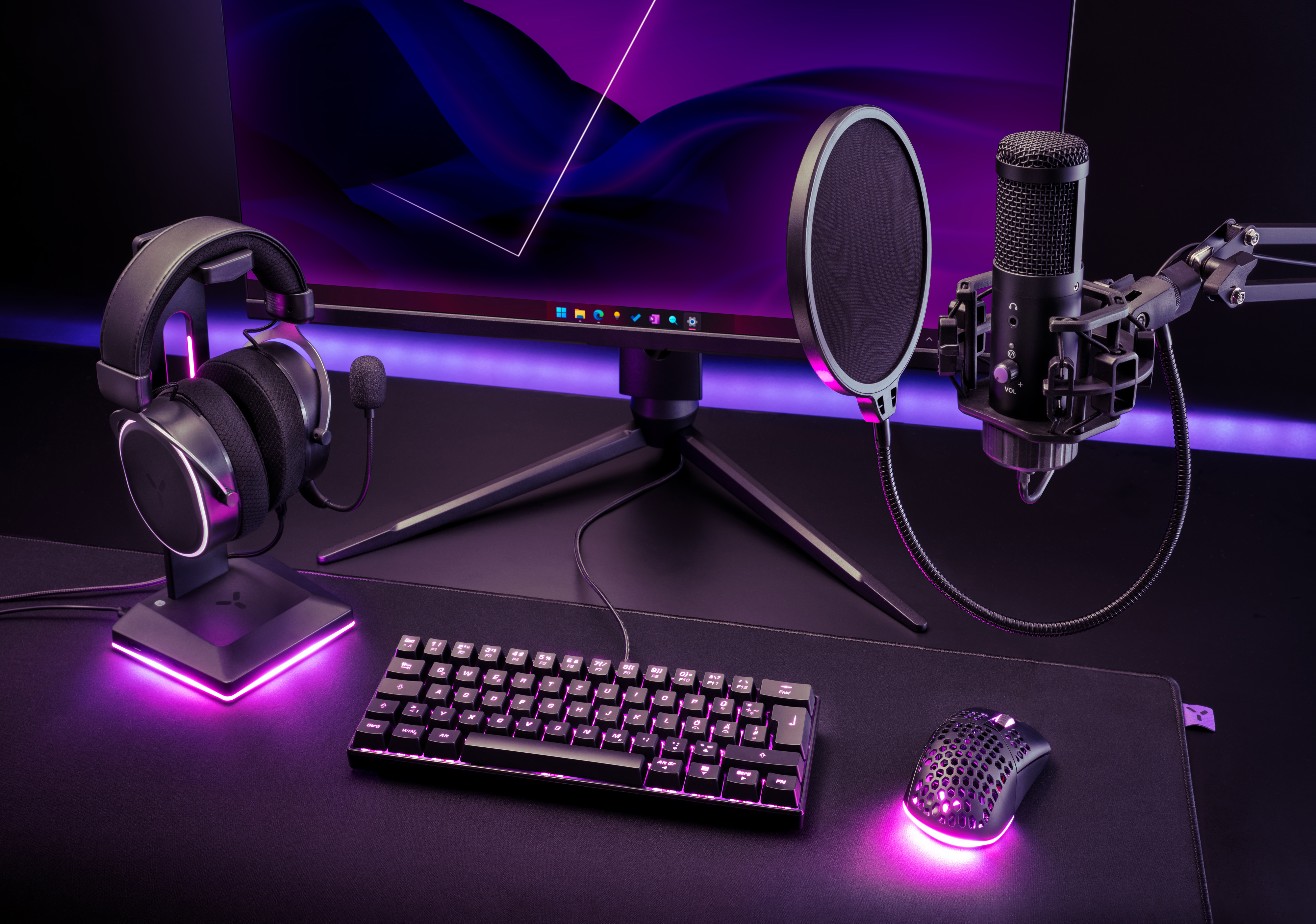 Gaming-Setup mit Kopfhörern, Mikrofon, Tastatur, Maus und Monitor auf einem schwarzen Schreibtisch.