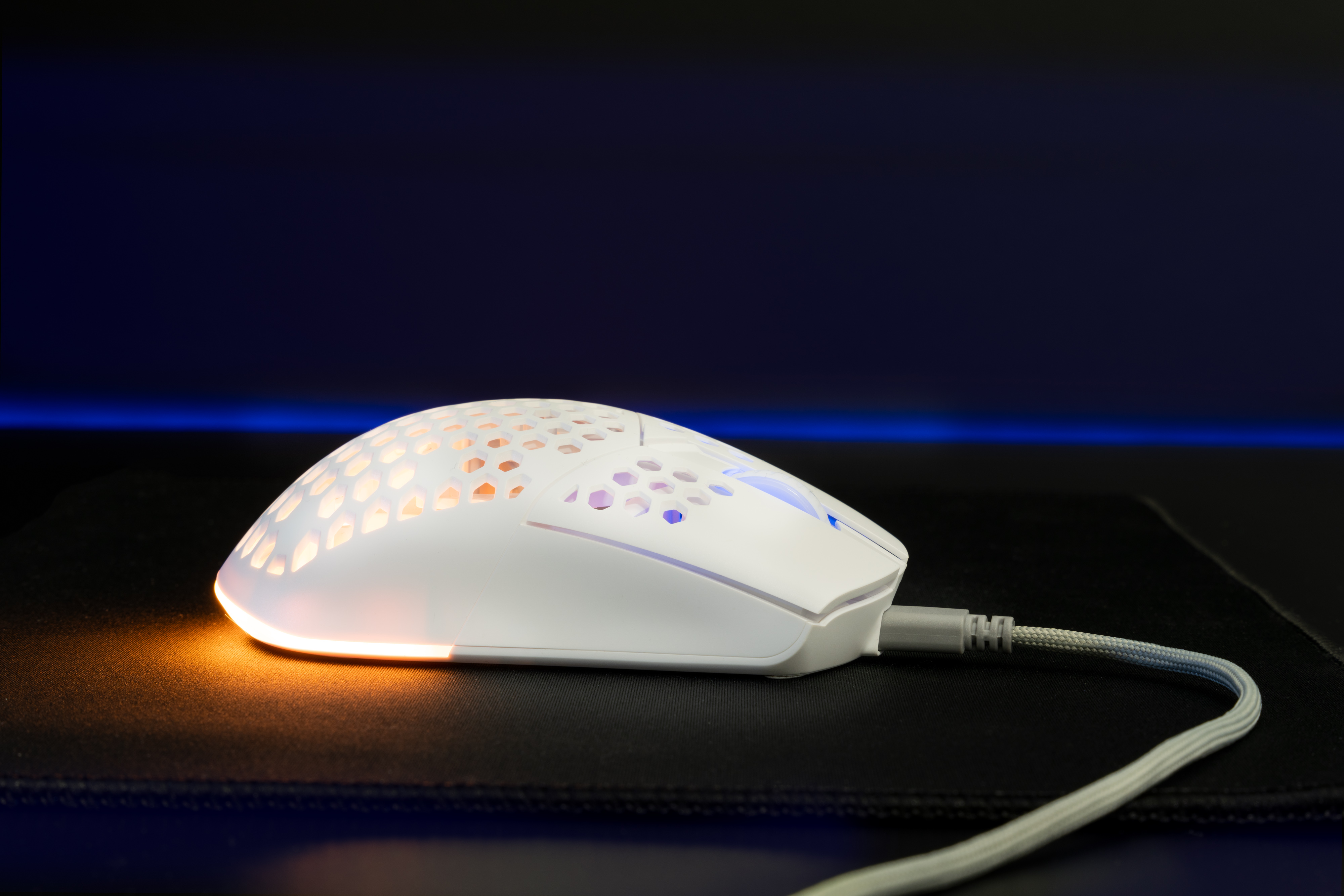 Une souris de jeu blanche sur un tapis de souris noir. La souris a un motif en nid d'abeille et des lumières.