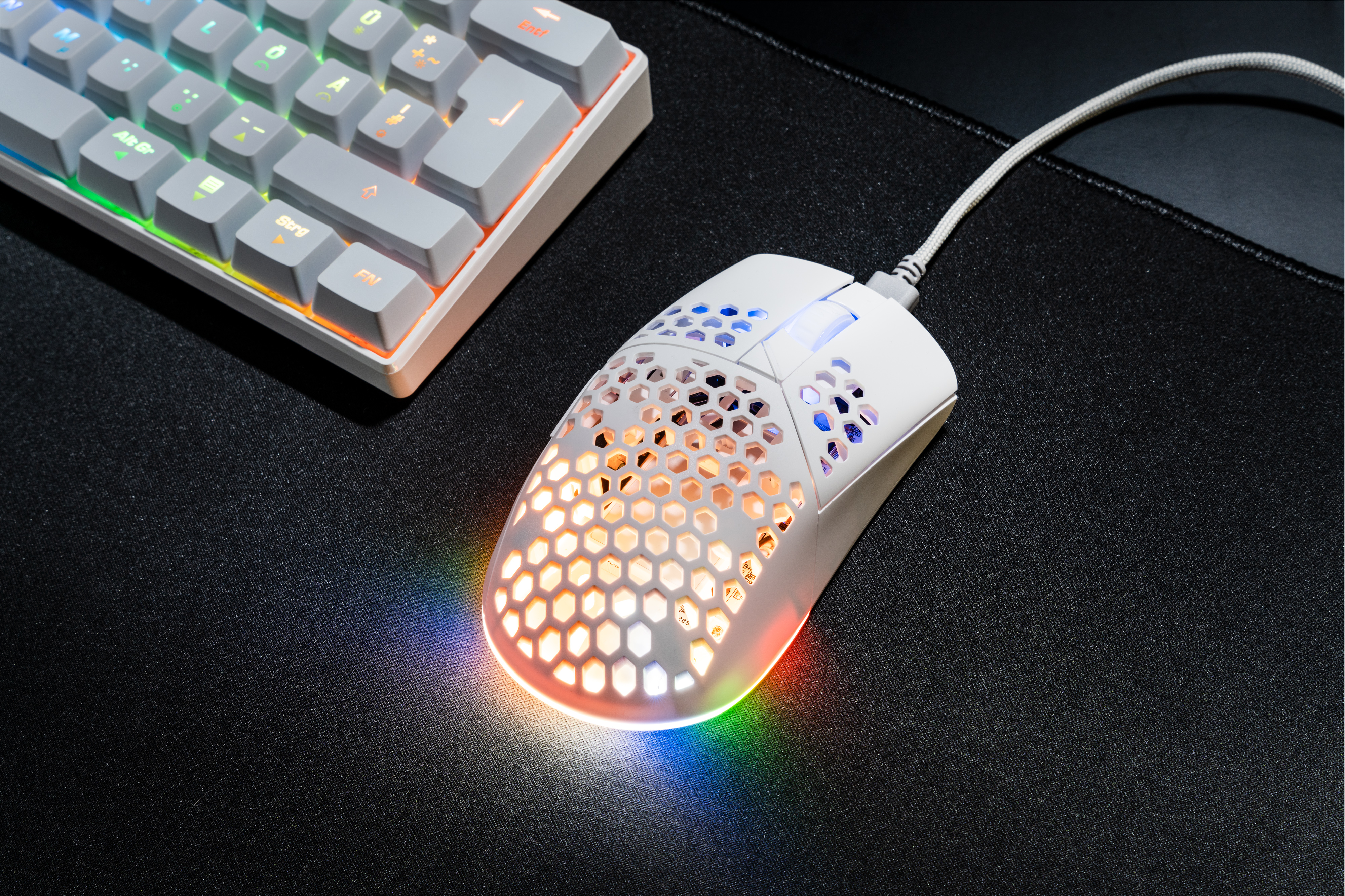 Souris de jeu blanche avec design en nid d'abeille, éclairée par des lumières RVB, clavier en arrière-plan.