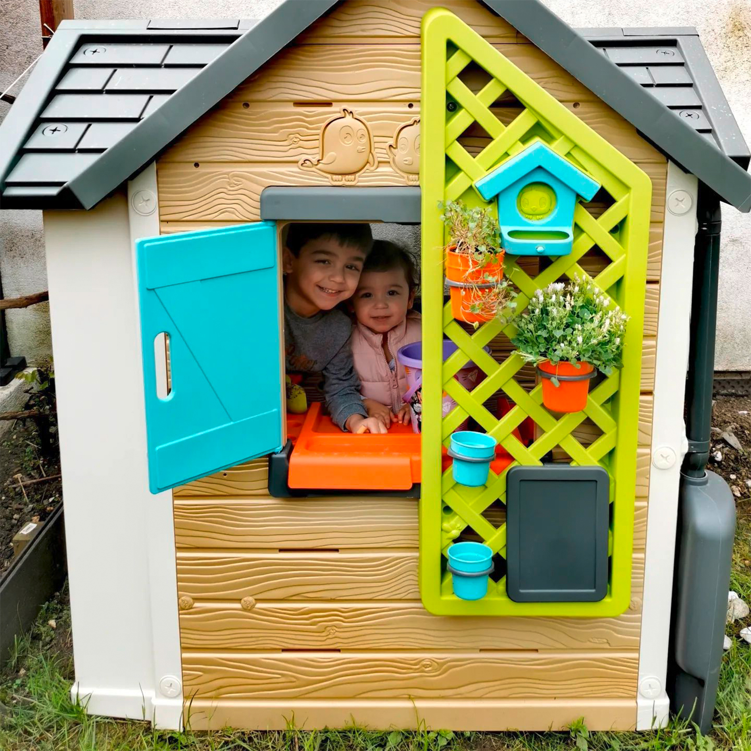 Due bambini in una casetta. Uno guarda fuori dalla finestra. La casa ha un traliccio verde.