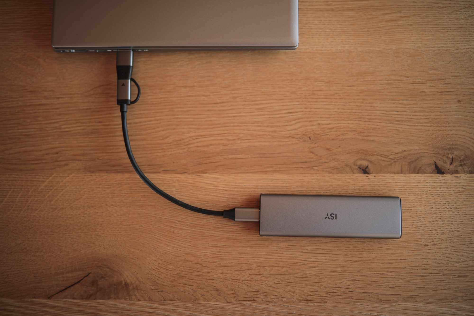 Srebrny koncentrator USB-C podłączony do laptopa i srebrnego urządzenia na drewnianym stole.