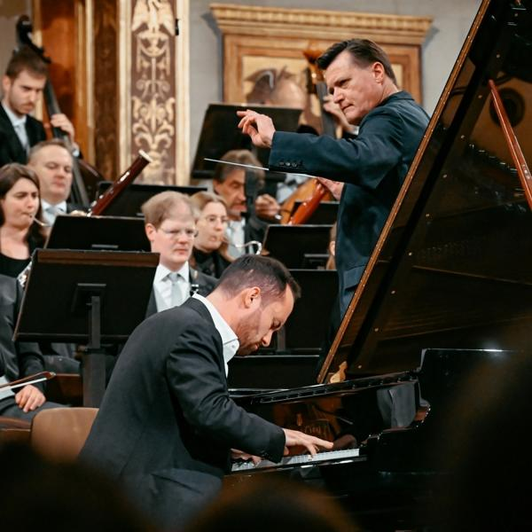 Dirigent dirigiert Orchester mit Klavier. Ein Mann spielt Klavier.
