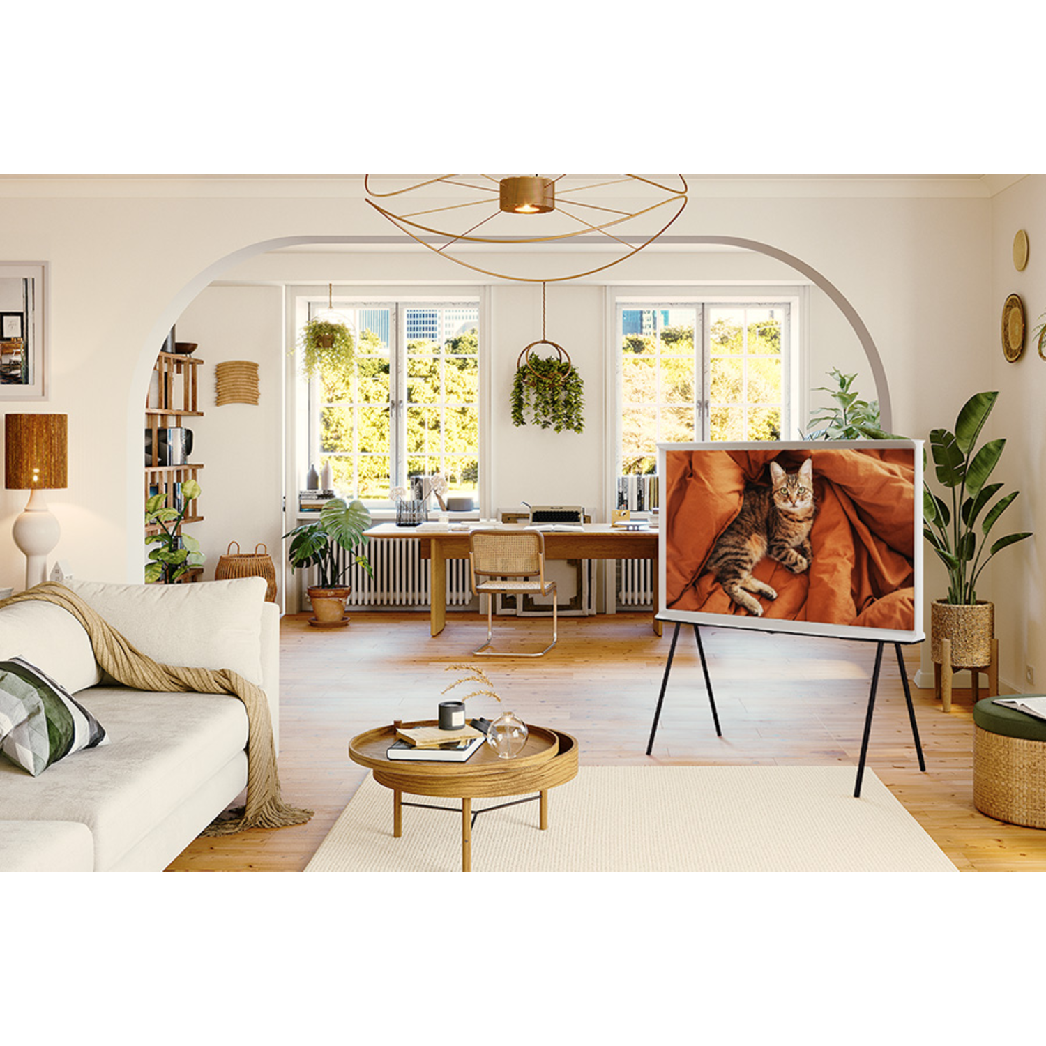 A living room with a TV showing a cat. A white couch, wooden table, plants, and windows are visible. The room is well-lit.