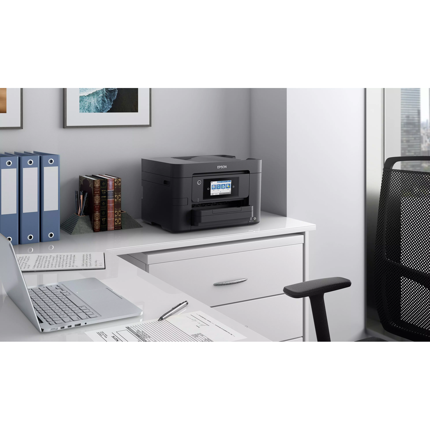 Black printer on a white desk with books, papers, and a laptop.