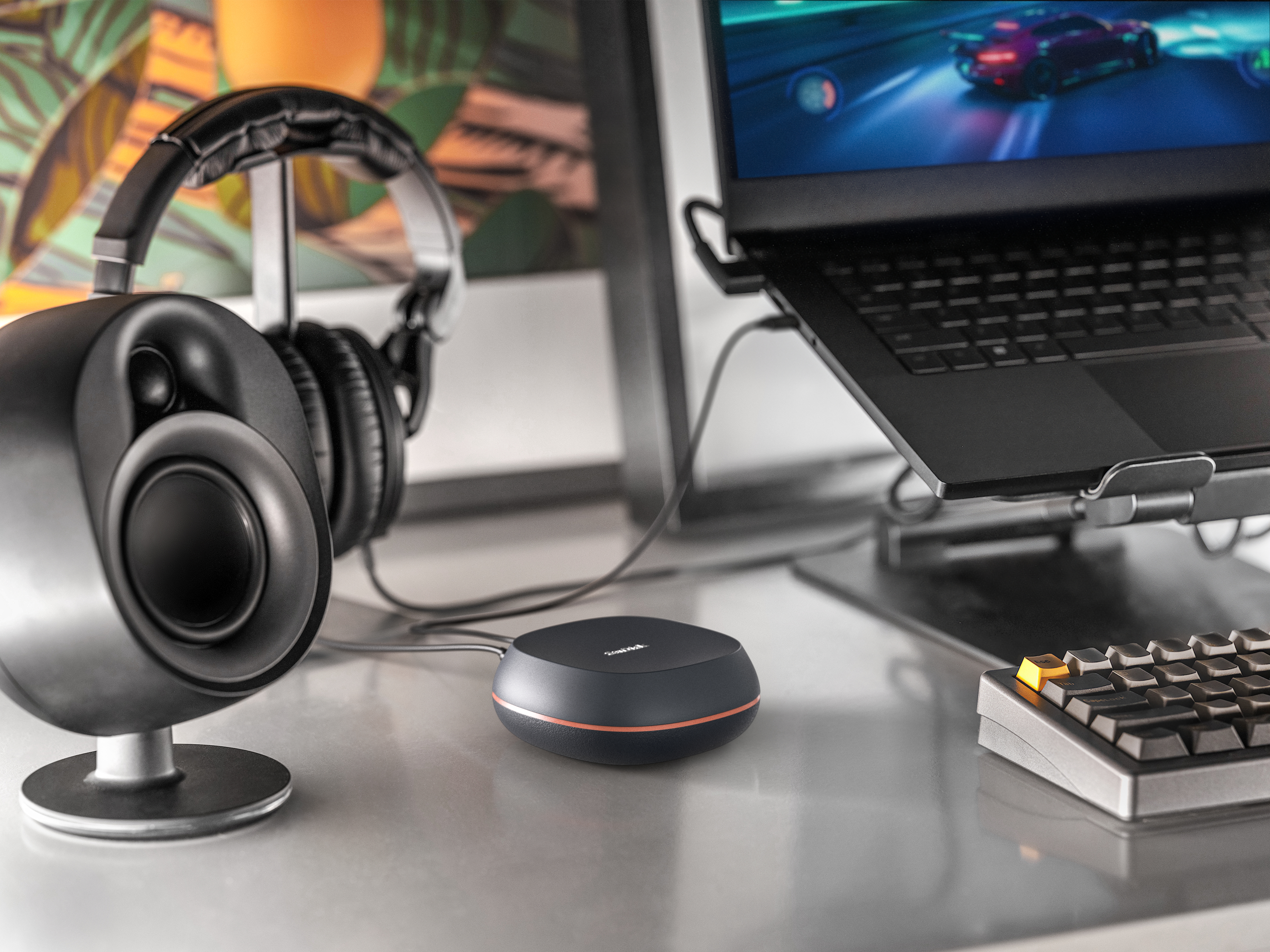 Ein Schreibtisch-Setup mit Kopfhörern, einem Lautsprecher, einem Laptop und einem schwarzen Audiogerät.