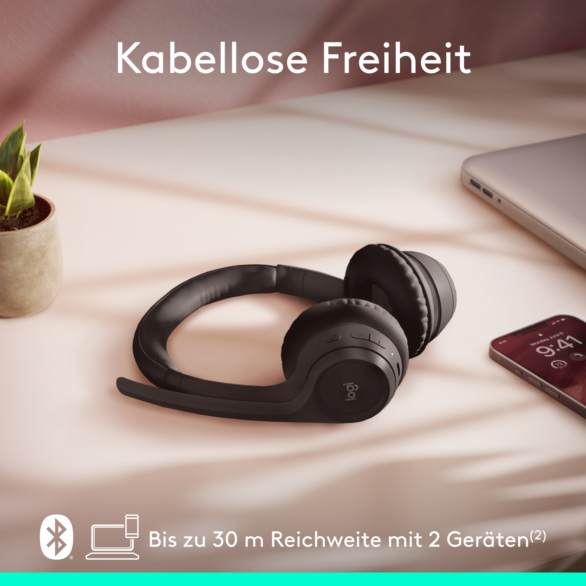 Schwarze Kopfhörer auf einer rosa Oberfläche. Ein Laptop und ein Telefon sind ebenfalls sichtbar.
