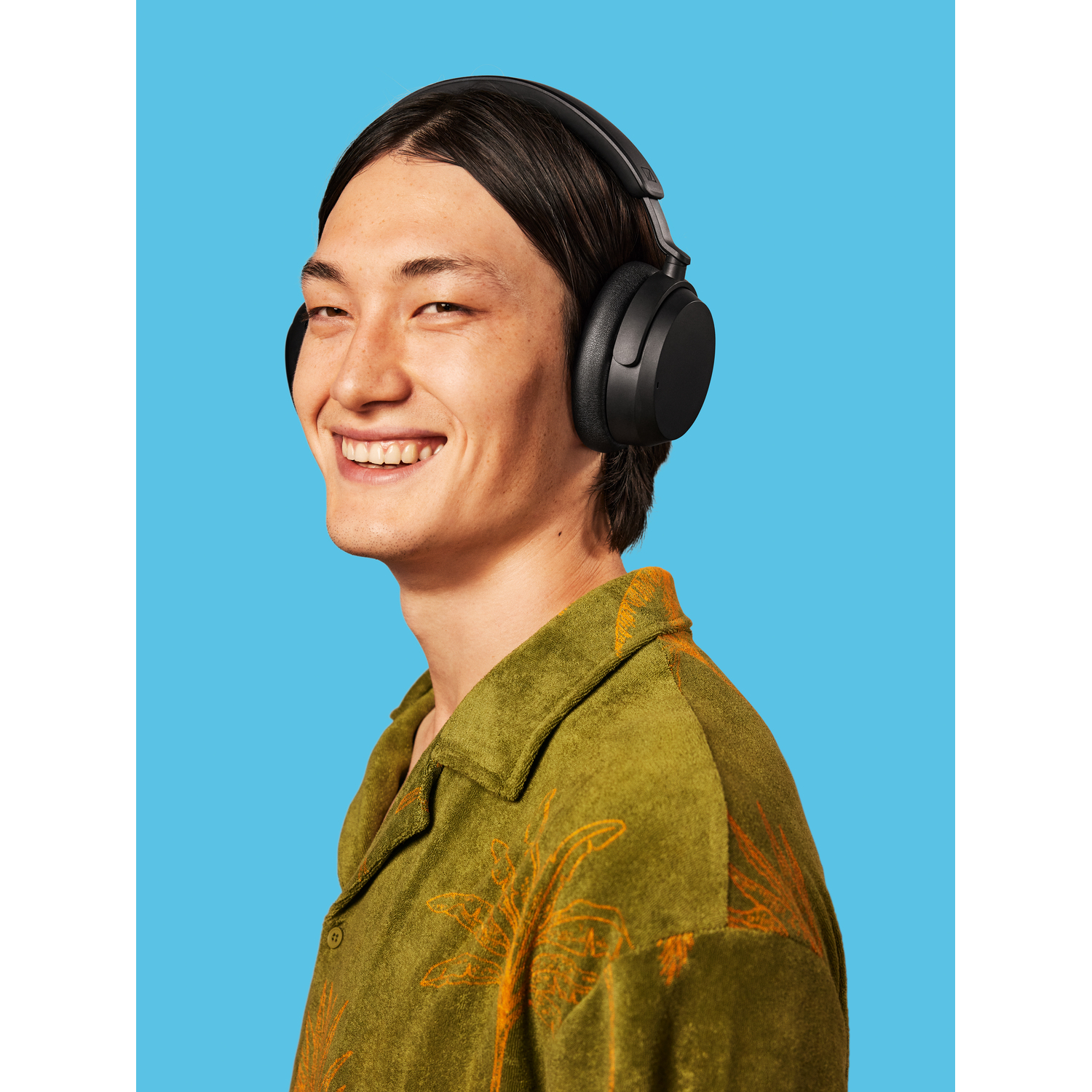 Un homme portant un casque sourit. Fond bleu. Chemise verte.