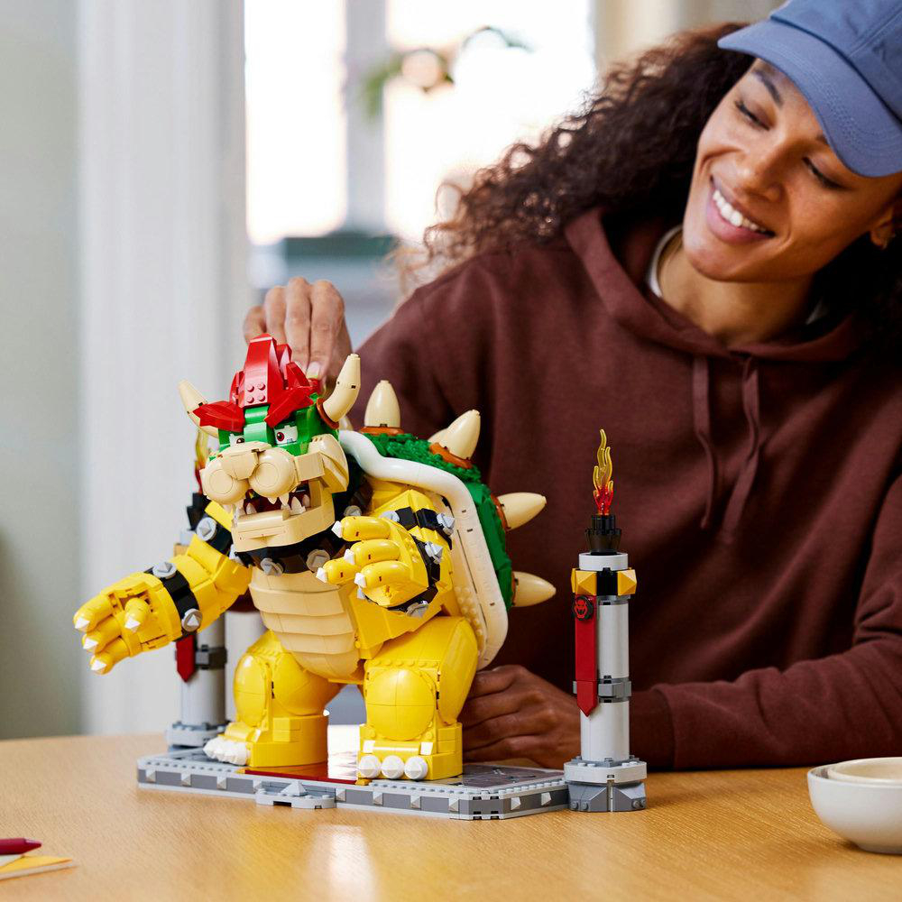 Frau, die eine Lego Bowser-Figur mit lächelndem Gesicht zusammensetzt, auf einem Tisch mit weißer Schüssel und Turm.