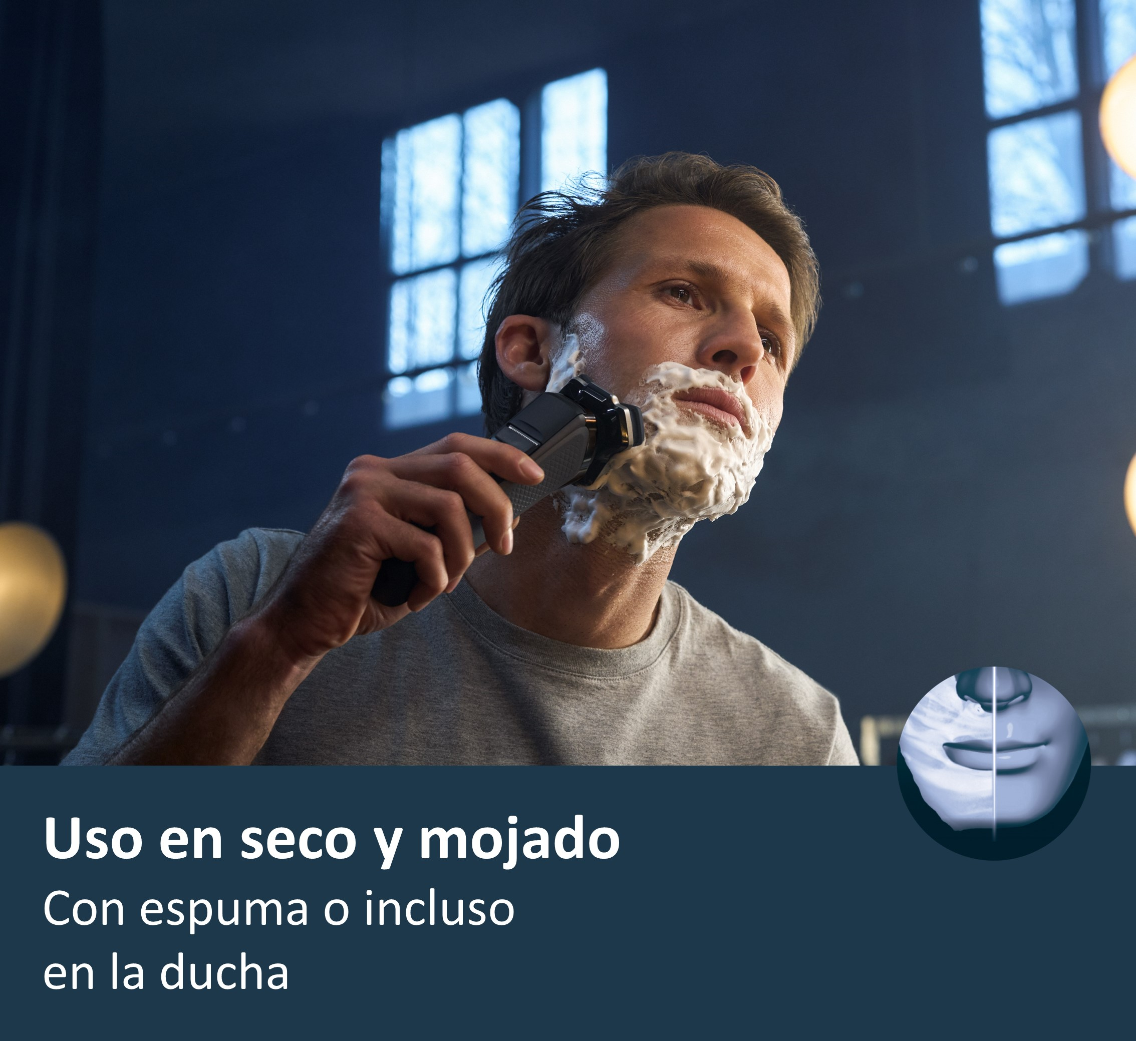 Hombre se afeita con afeitadora negra, espuma blanca en la cara. En el fondo, un área azul oscuro con luces.