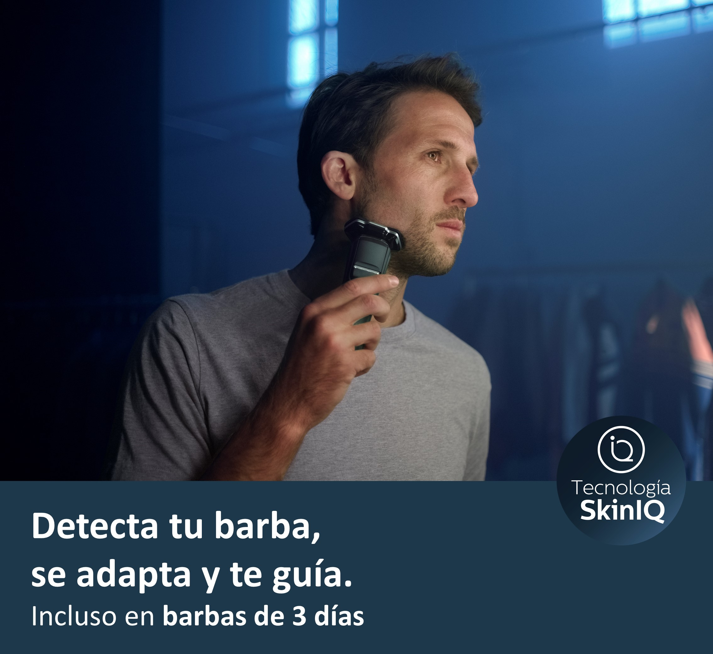 Hombre afeitándose con una afeitadora eléctrica en un baño con luz azul oscura.